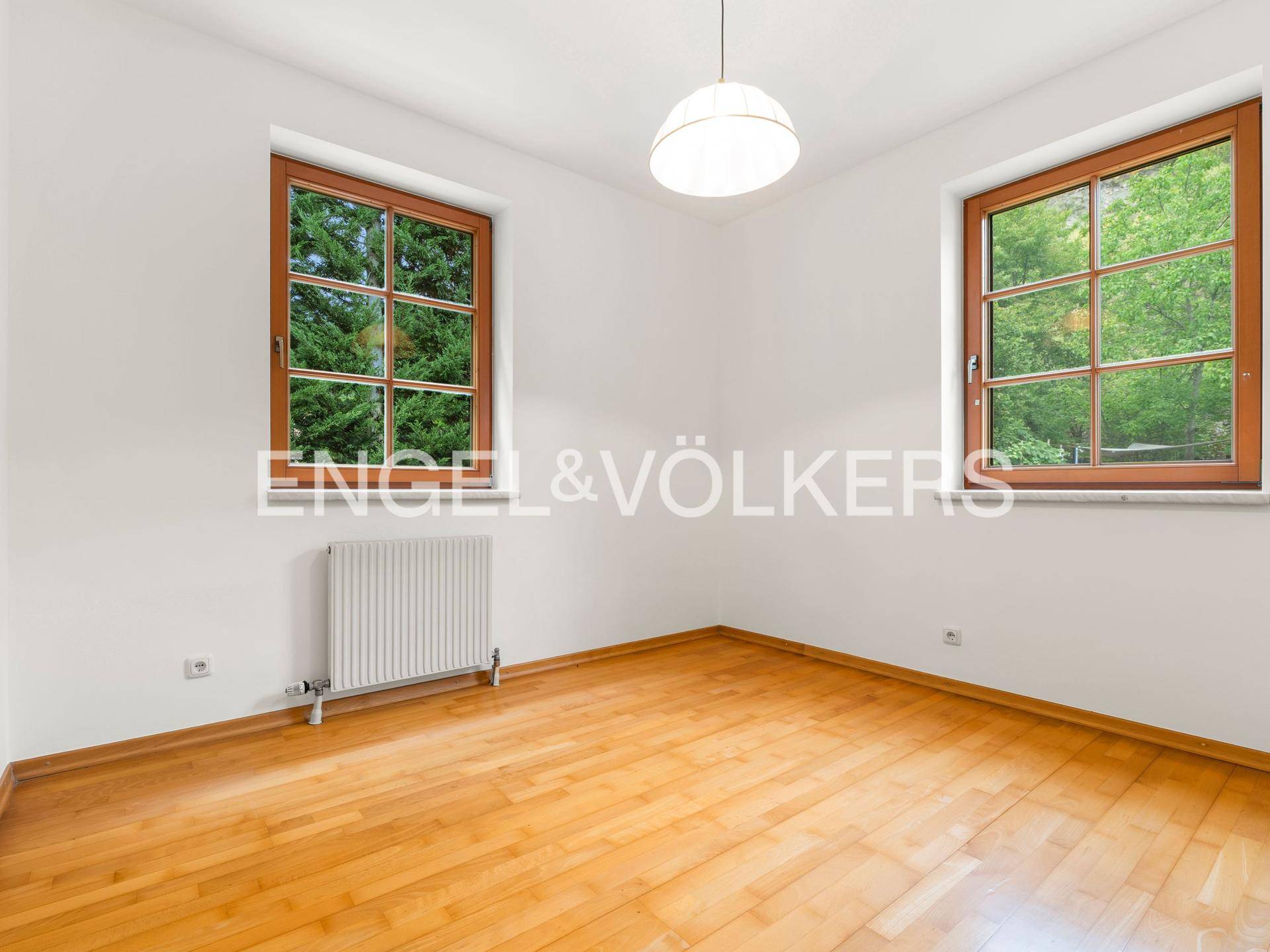 Helles Schlafzimmer mit Parkettboden, zwei Fenstern und einem angenehmen Blick ins Grüne.
