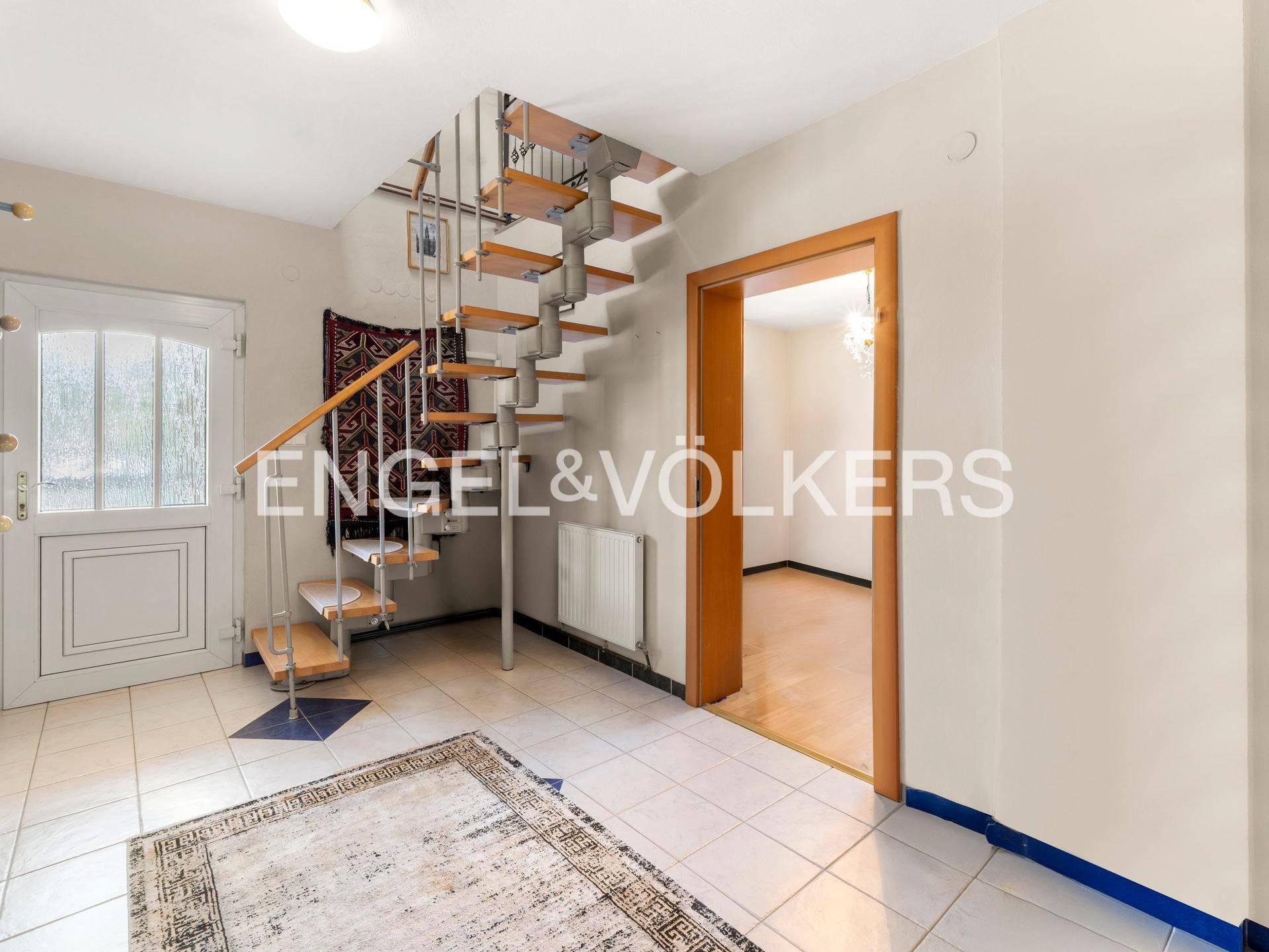 Eingangsbereich mit heller Fliesenboden und einer eleganten Wendeltreppe zum Obergeschoss.
