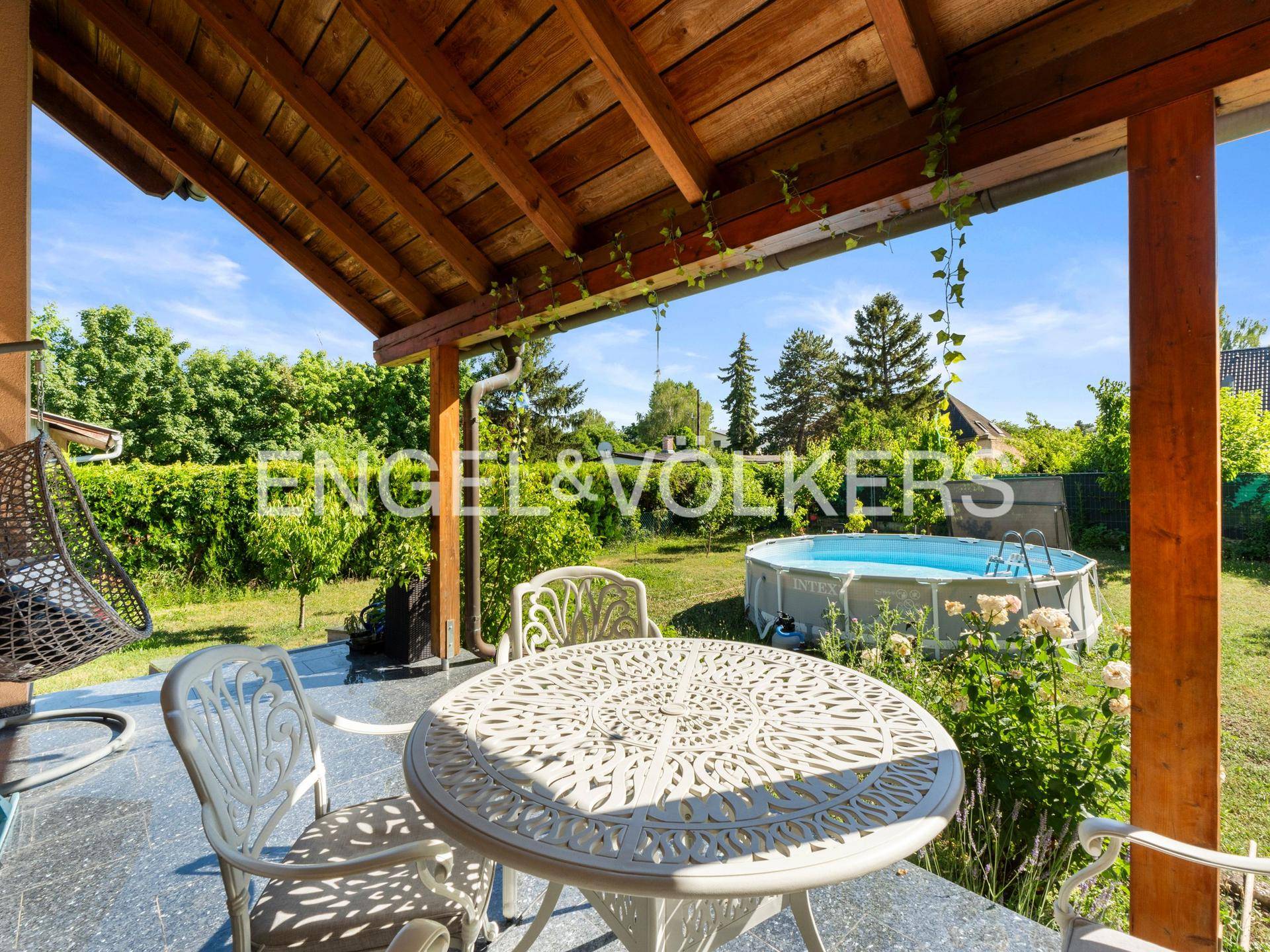 Überdachte Terrasse mit Gartenmöbeln und Blick auf den Pool und den Garten.