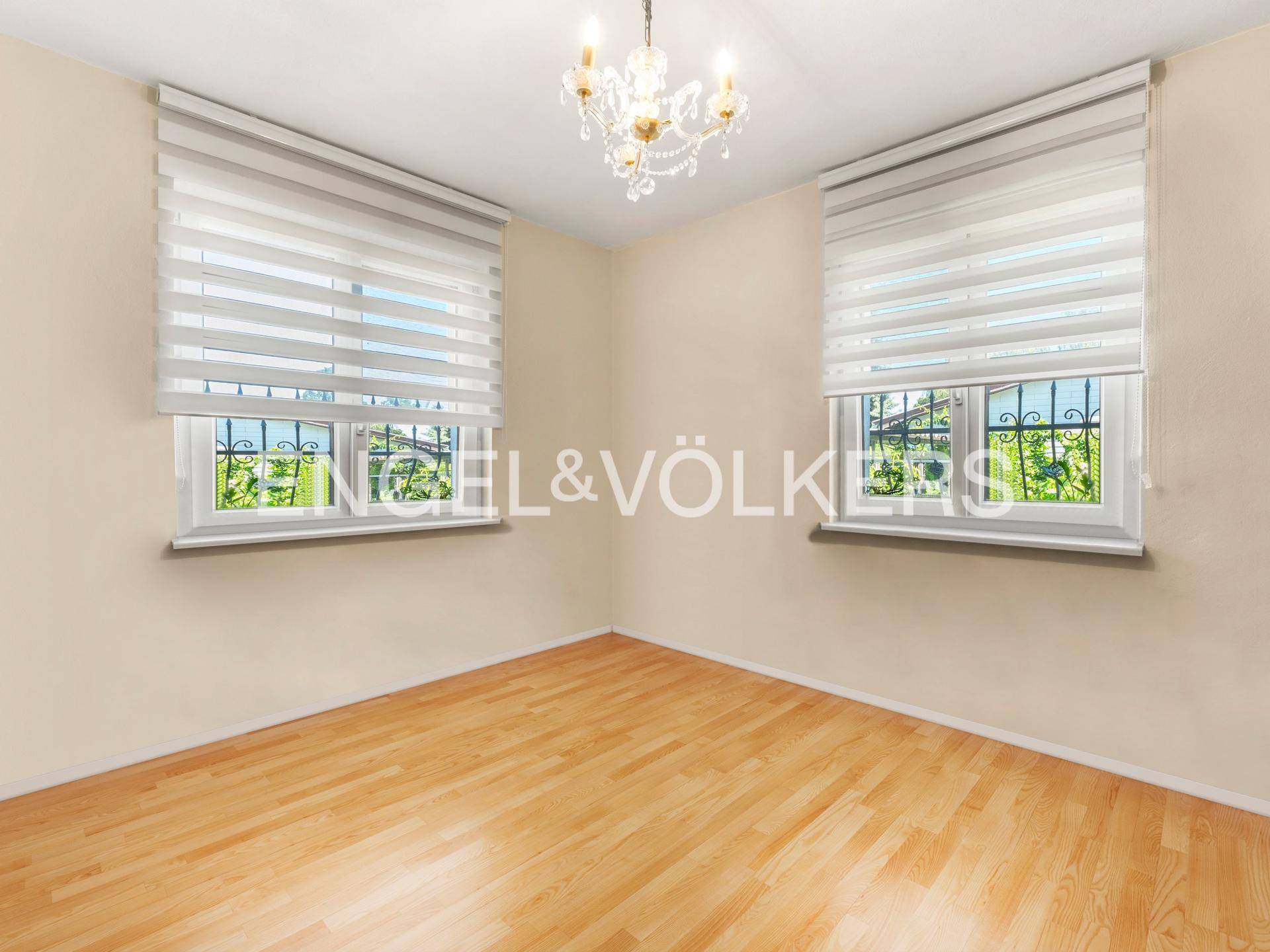 Helles Zimmer mit Holzboden, zwei Fenstern und einem eleganten Kronleuchter.