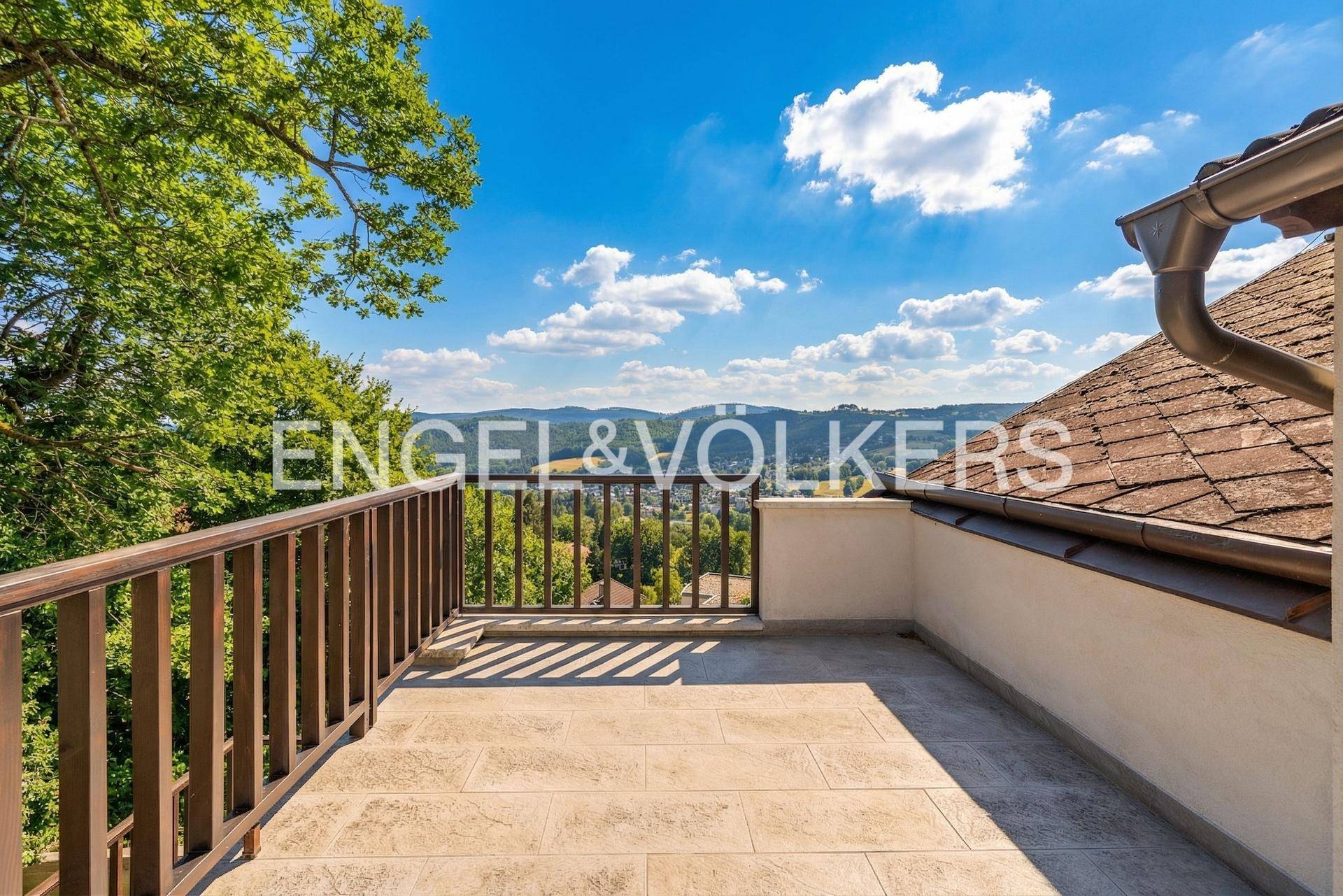 Sonniger Dachbalkon mit Fliesenboden und Panoramablick über die umliegende Landschaft.