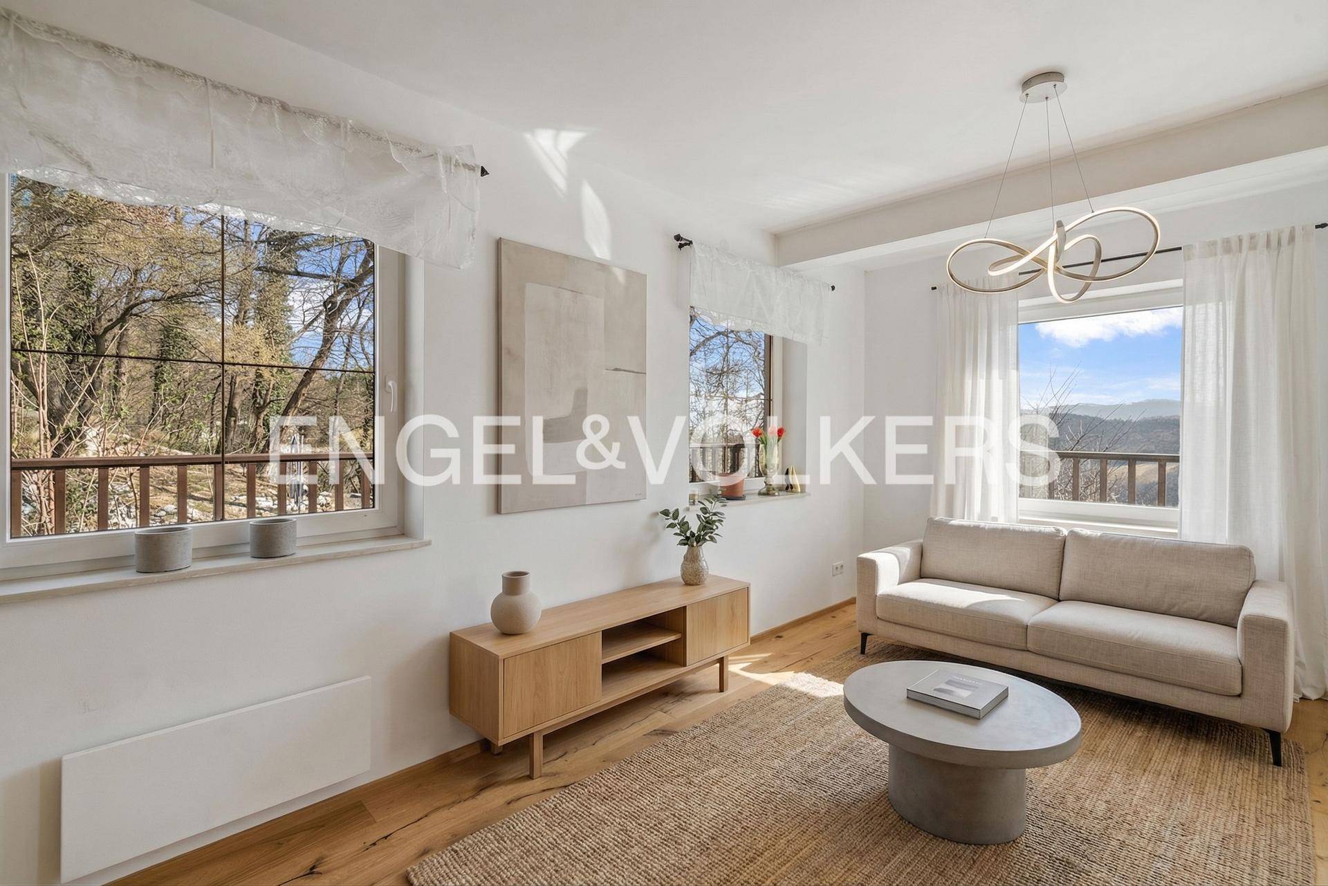 Helles Wohnzimmer mit modernem Sofa, Holzboden und großen Fenstern mit Weitblick.