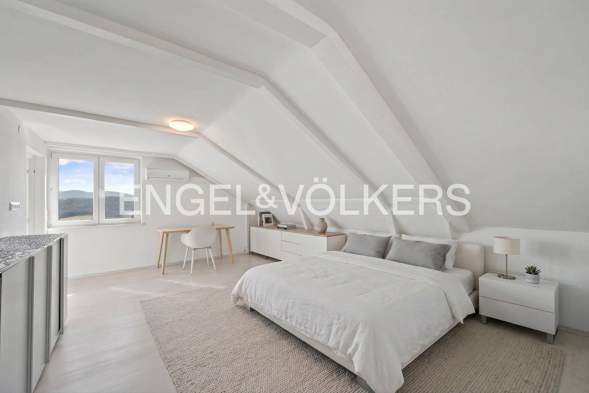 Helles Schlafzimmer im Dachgeschoss mit schrägen Wänden, Holzboden und Blick ins Grüne.