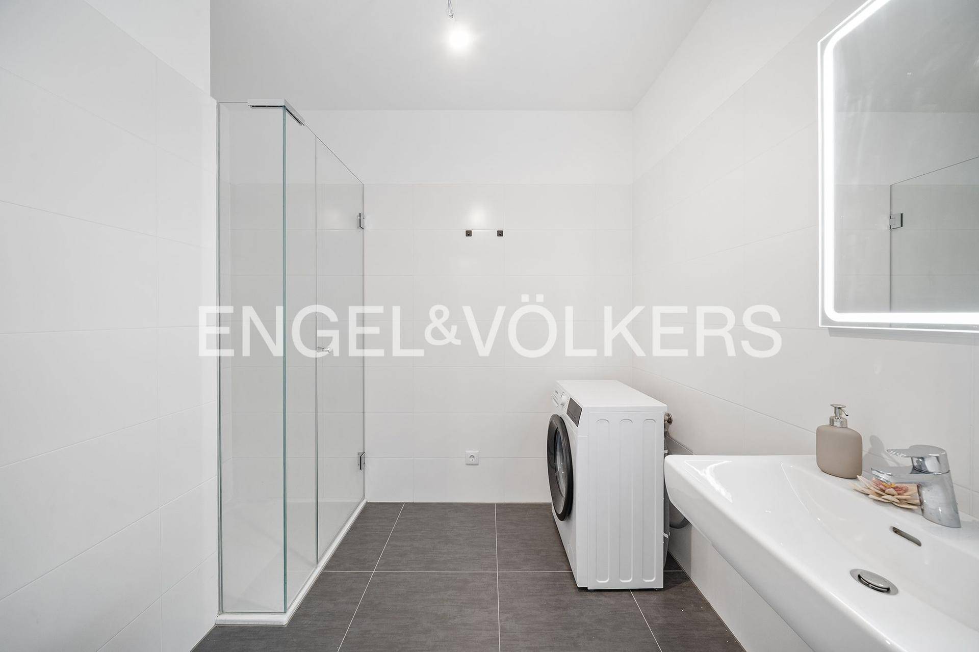 Modernes Badezimmer mit Dusche, Waschbecken, beleuchtetem Spiegel und Waschmaschine.
