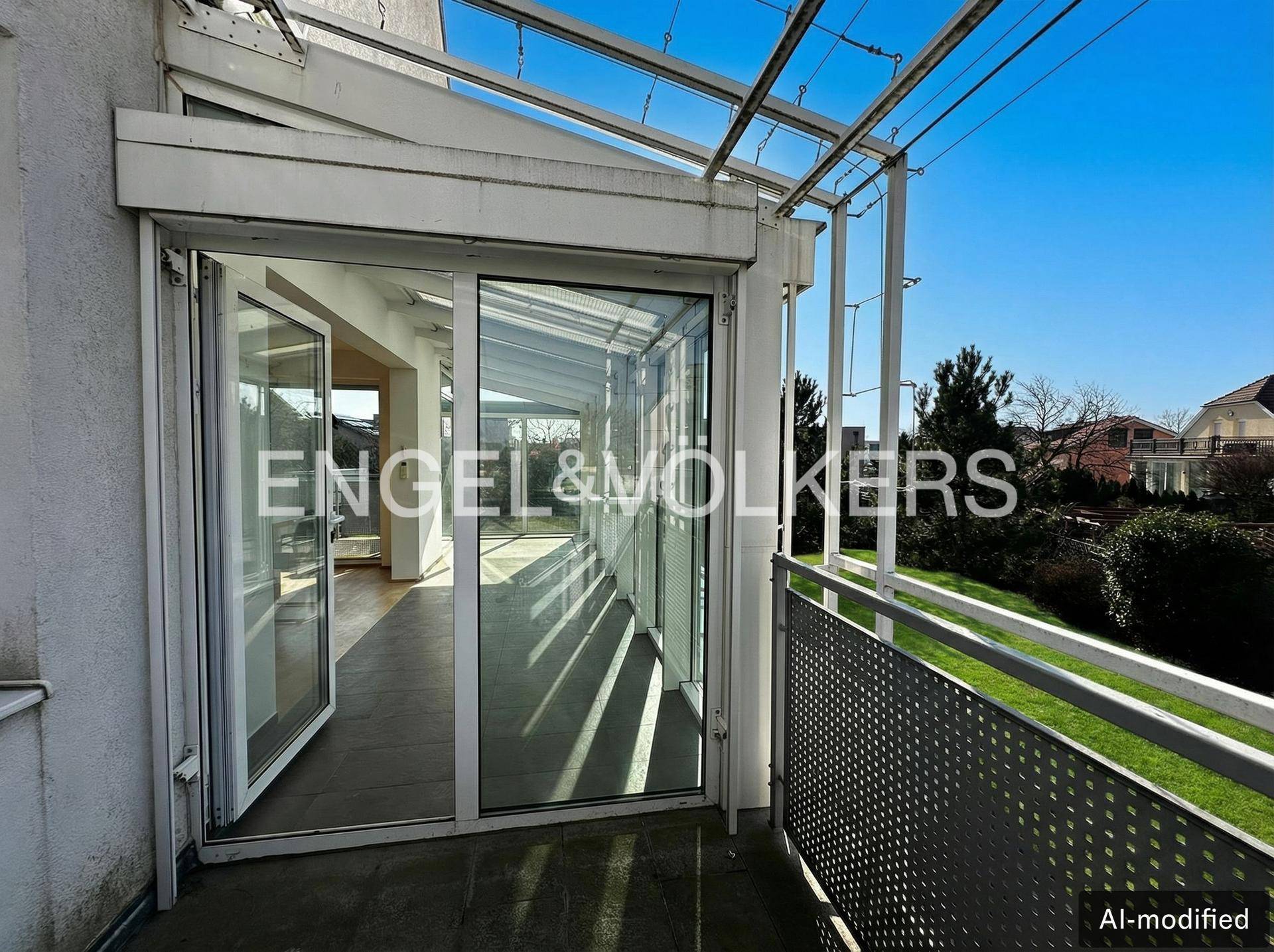 Balkon mit Blick auf den Wintergarten und die umliegende grüne Landschaft an einem sonnigen Tag.