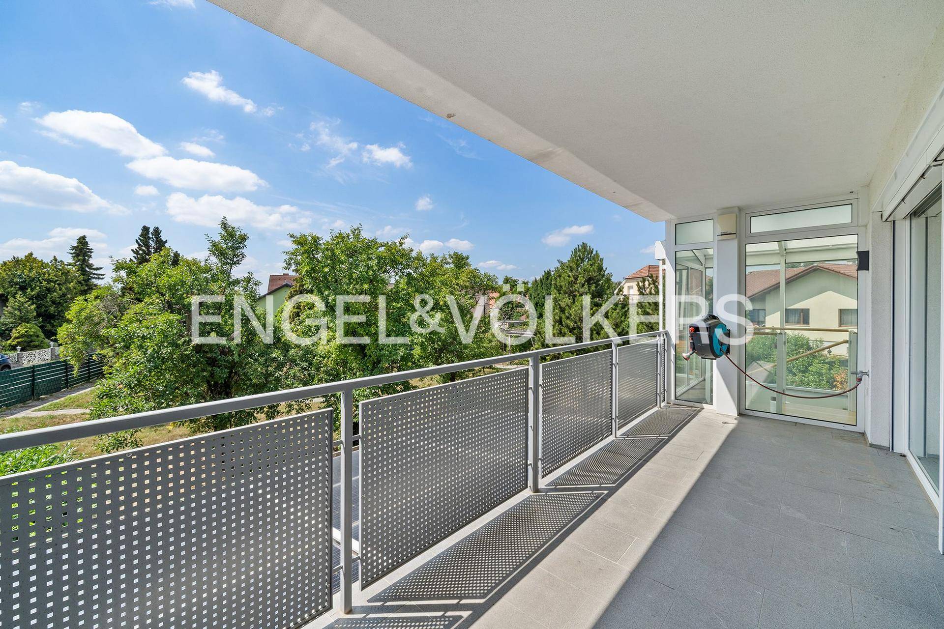 Geräumiger Balkon mit Metallgeländer und weitem Blick ins Grüne unter blauem Himmel.