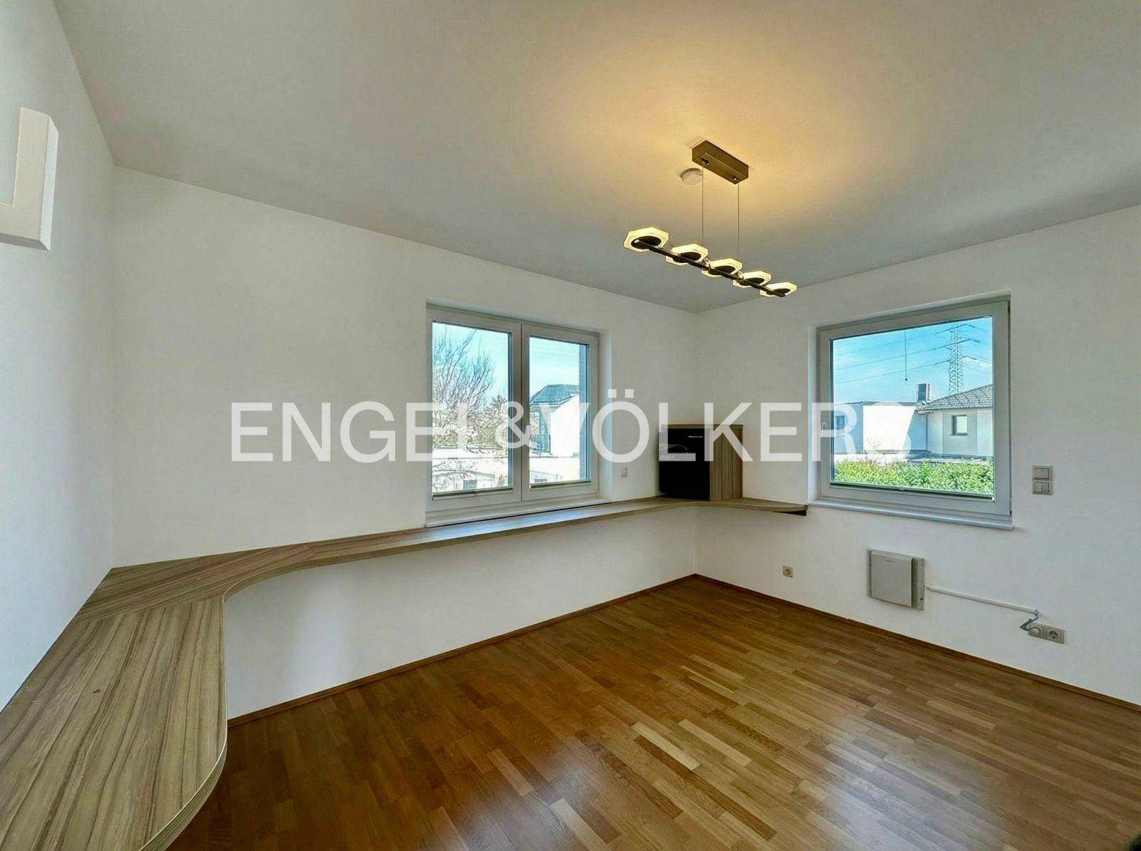 Helles Zimmer mit Holzboden, großen Fenstern und einem integrierten Schreibtischbereich.