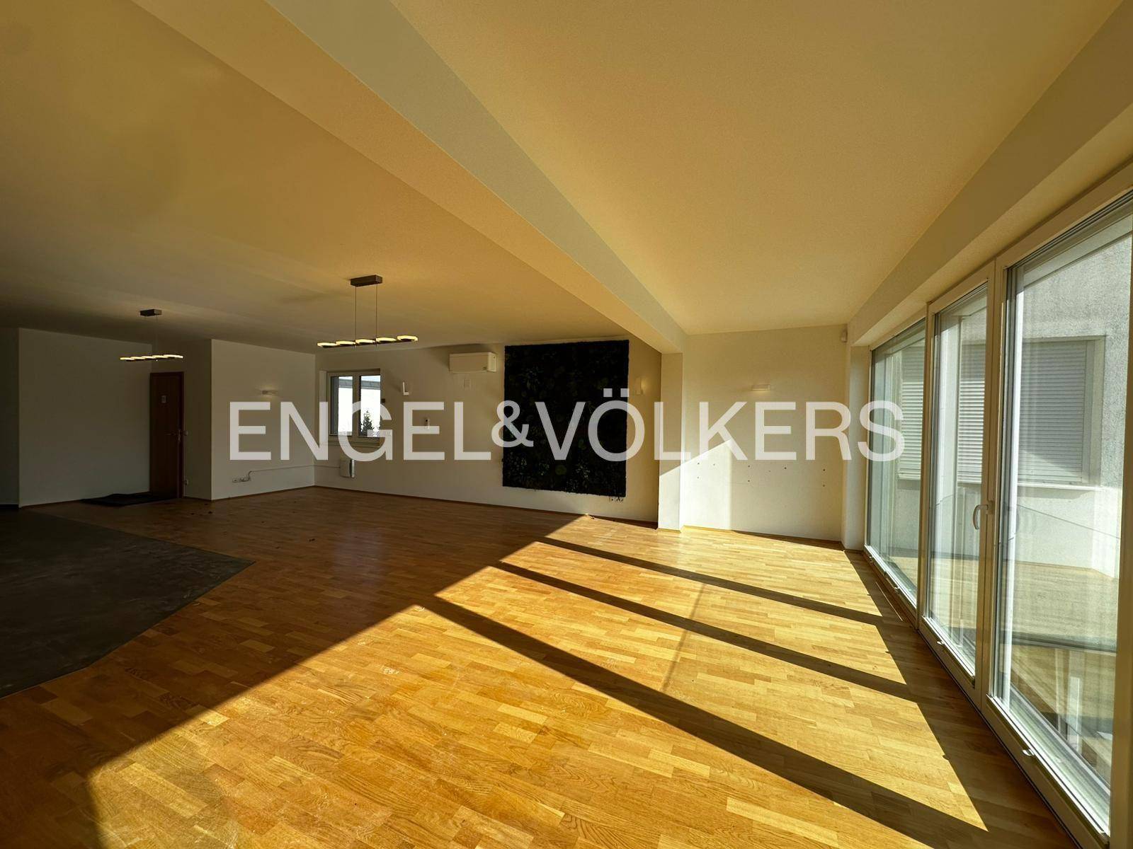 Lichtdurchfluteter Wohnbereich mit Holzboden und großen Fensterfronten, die viel Sonne bieten.