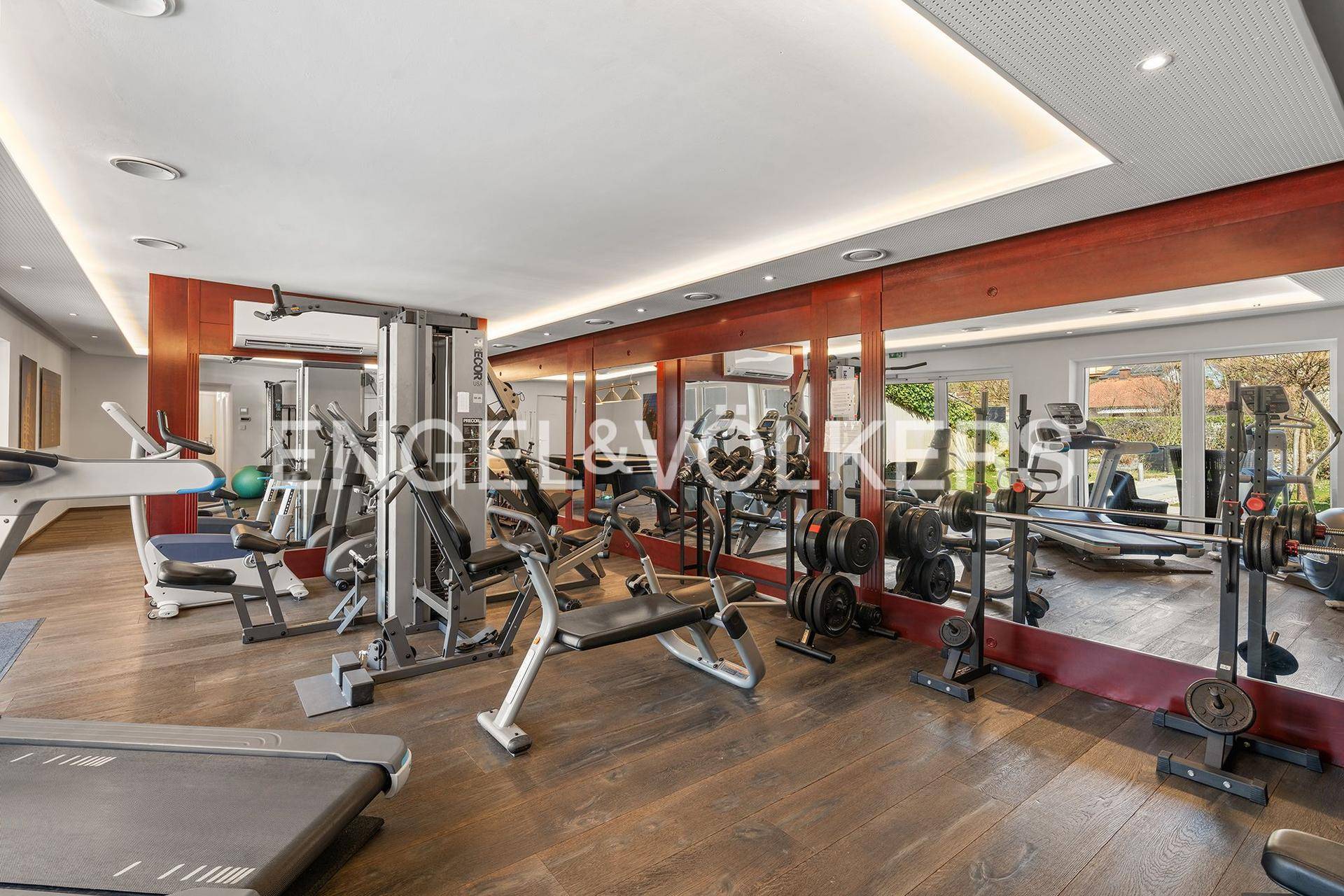Gut ausgestatteter Fitnessraum mit verschiedenen Trainingsgeräten und großen Spiegeln.