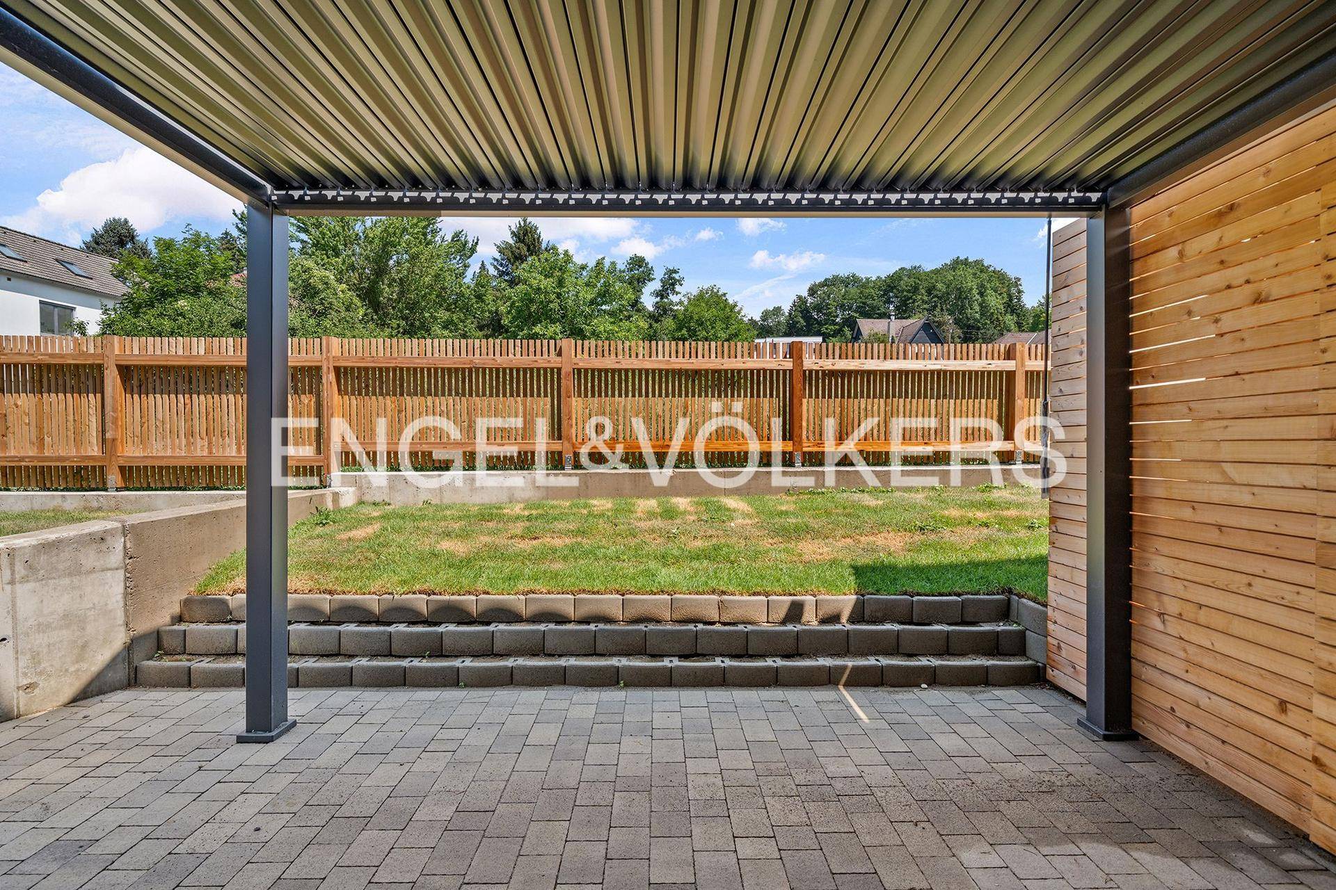 Überdachte Terrasse mit Pflastersteinen und Blick auf den Gartenbereich.