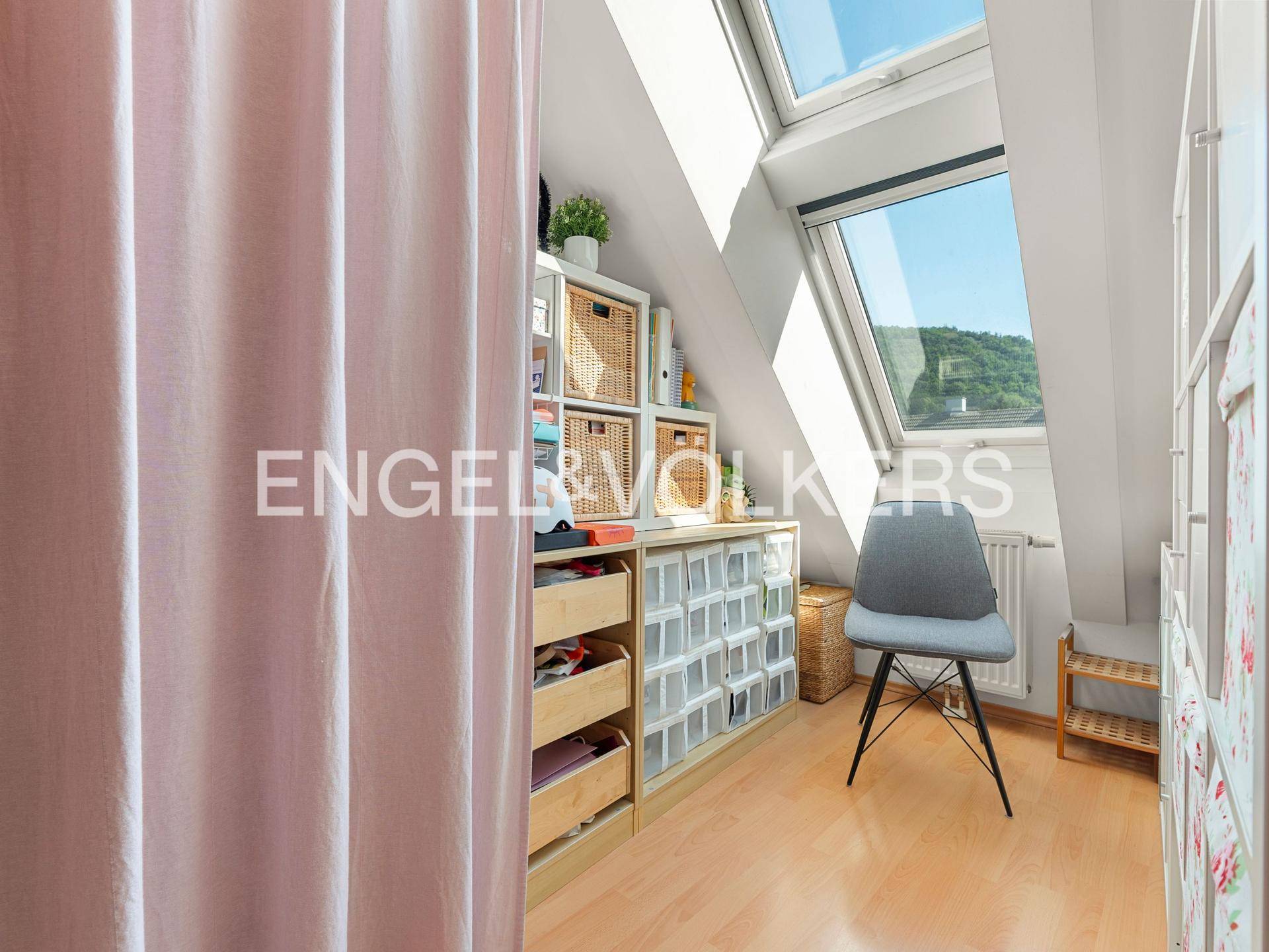 Helles Zimmer im Dachgeschoss mit Schrägdach, Dachfenstern und praktischen Aufbewahrungsmöbeln.
