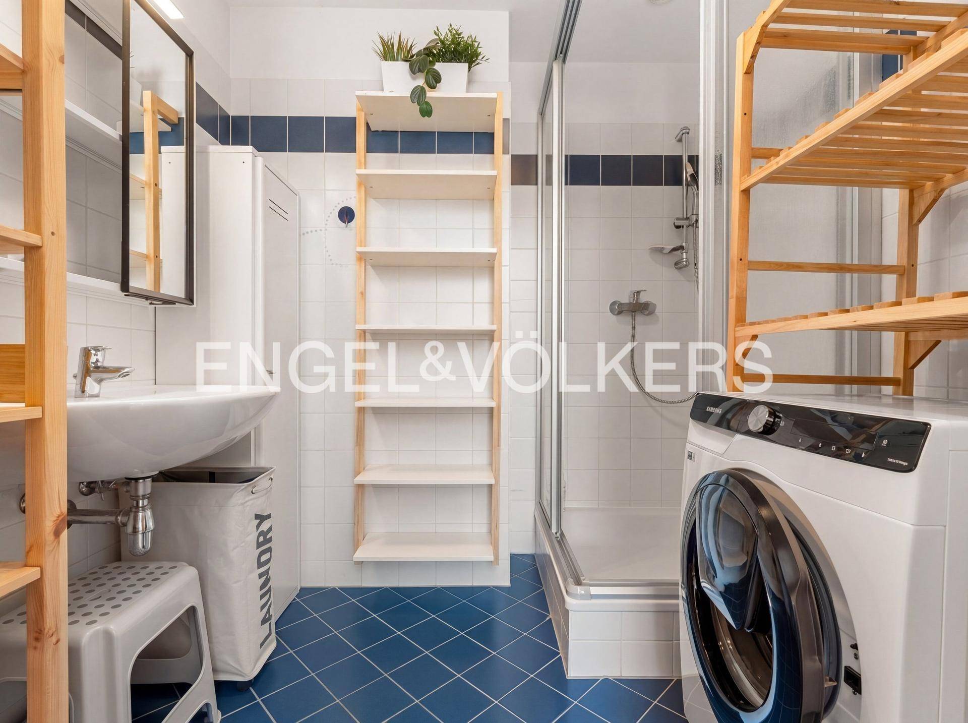 Badezimmer mit blauen und weißen Fliesen, Duschkabine, Waschbecken und Waschmaschine.