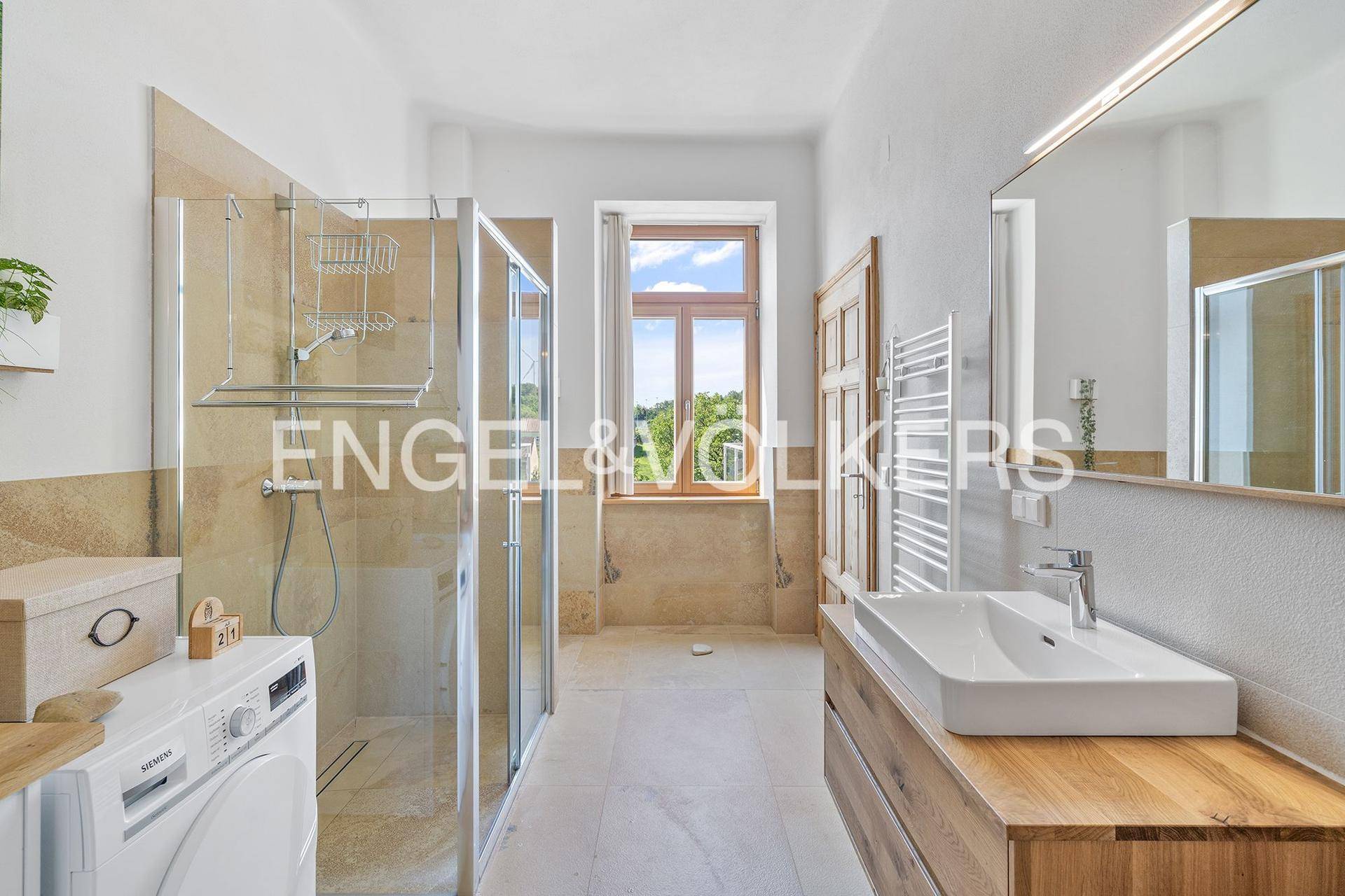 Helles Badezimmer mit moderner Dusche, Waschbecken auf Holzunterschrank und Fenster.