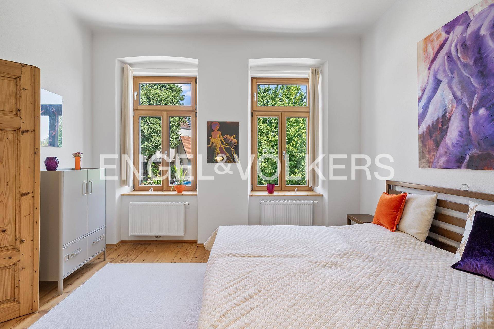 Helles Schlafzimmer mit Holzboden, großen Fenstern und Blick ins Grüne.