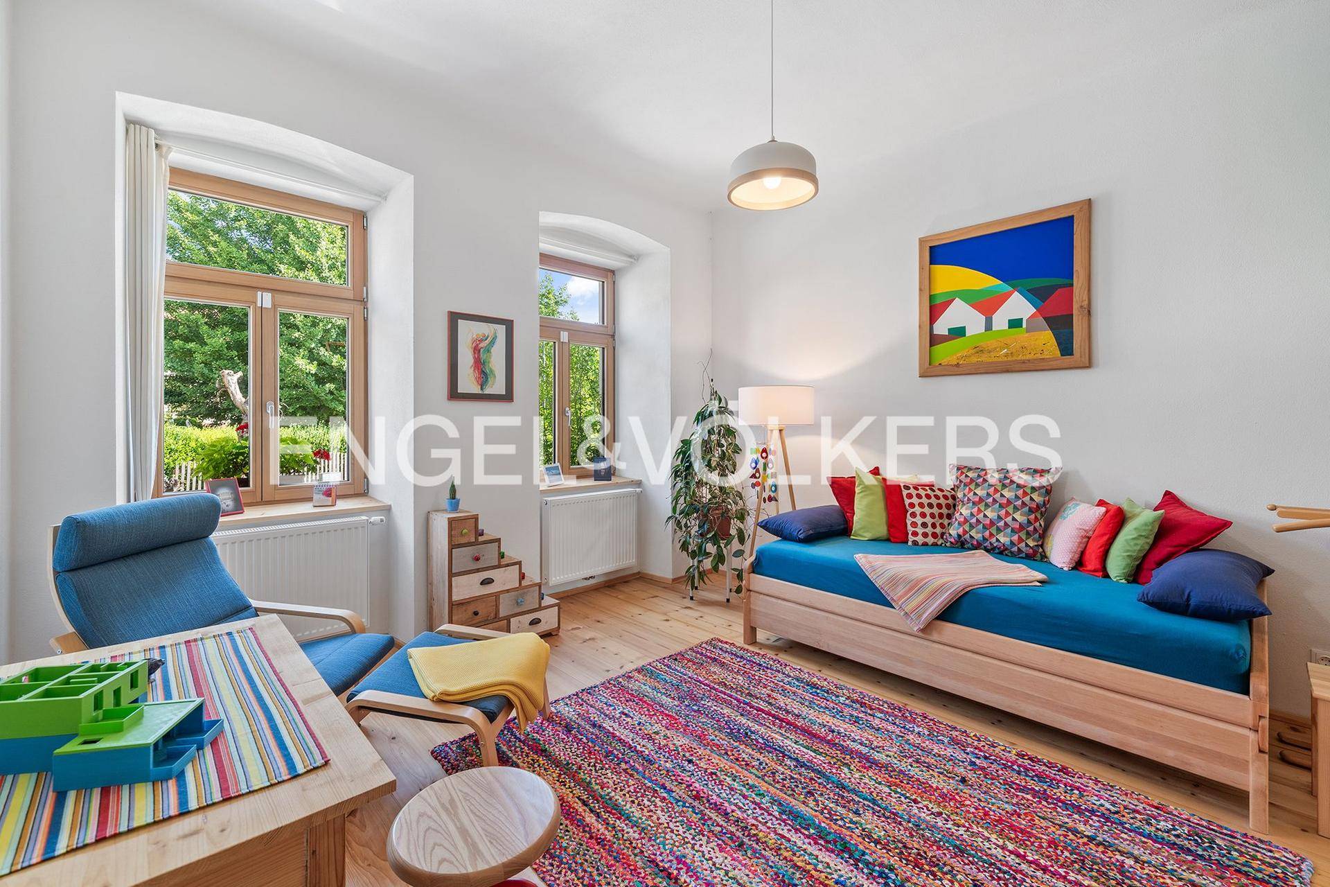 Gemütliches Wohnzimmer mit farbenfroher Dekoration, Holzboden und Blick in den Garten.