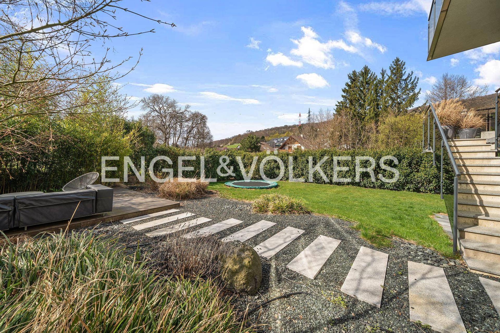 Gepflegter Gartenbereich mit Trampolin, Steinfliesenweg und Sitzgelegenheiten im Freien.