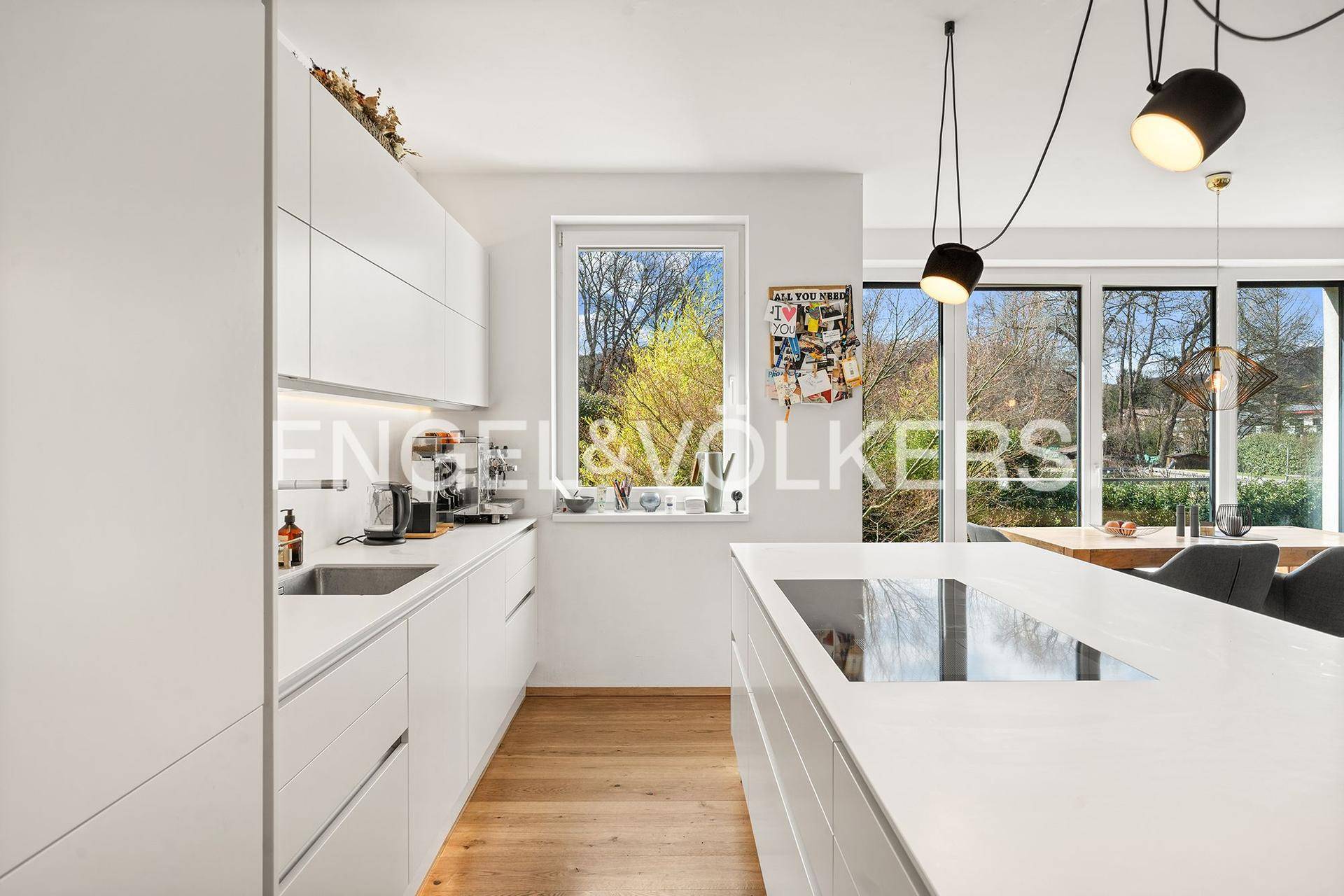 Moderne weiße Küche mit Kochinsel, Induktionskochfeld und viel Tageslicht.