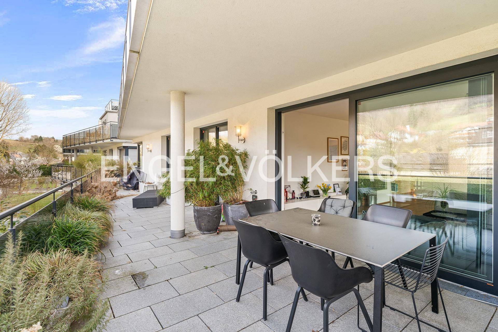 Geräumige Terrasse mit Steinfliesen, Esstisch und Blick auf die grüne Umgebung.