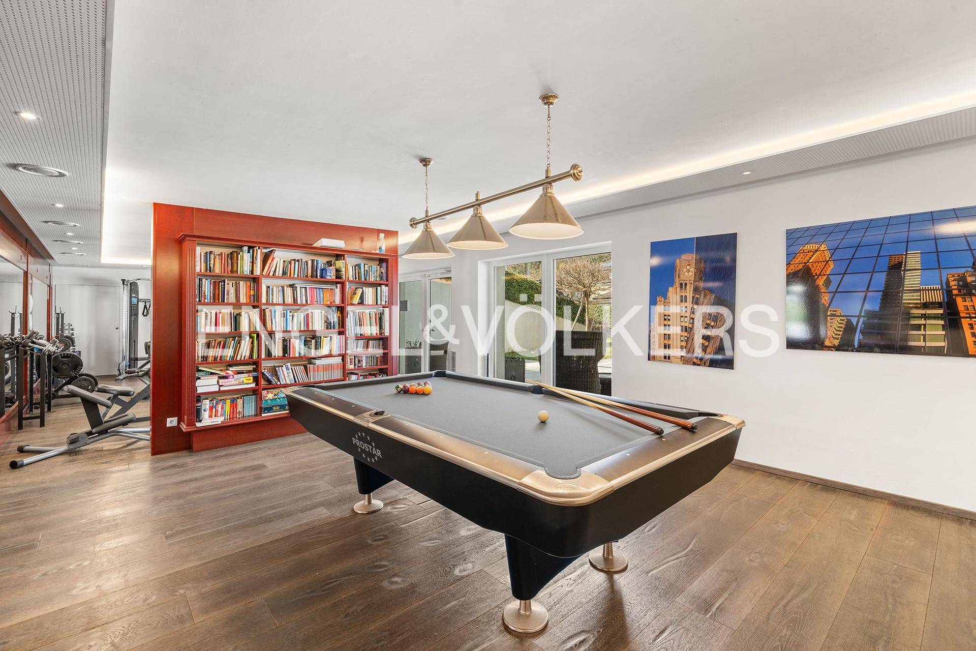 Geräumiger Freizeitraum mit Billardtisch, Bücherregal und Fitnessbereich.