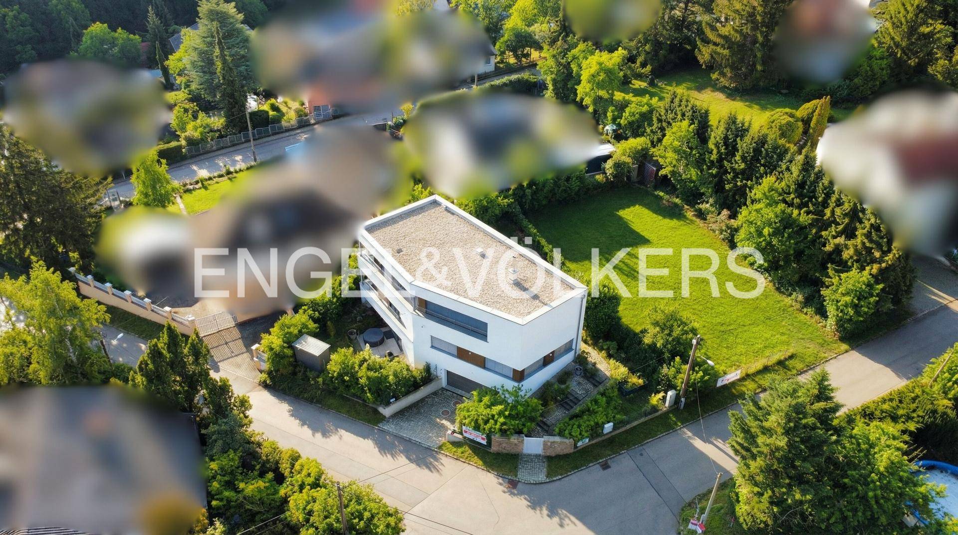 Panoramablick auf ein modernes, weißes Wohnhaus mit Flachdach, umgeben von viel Grün und weiteren Häusern.