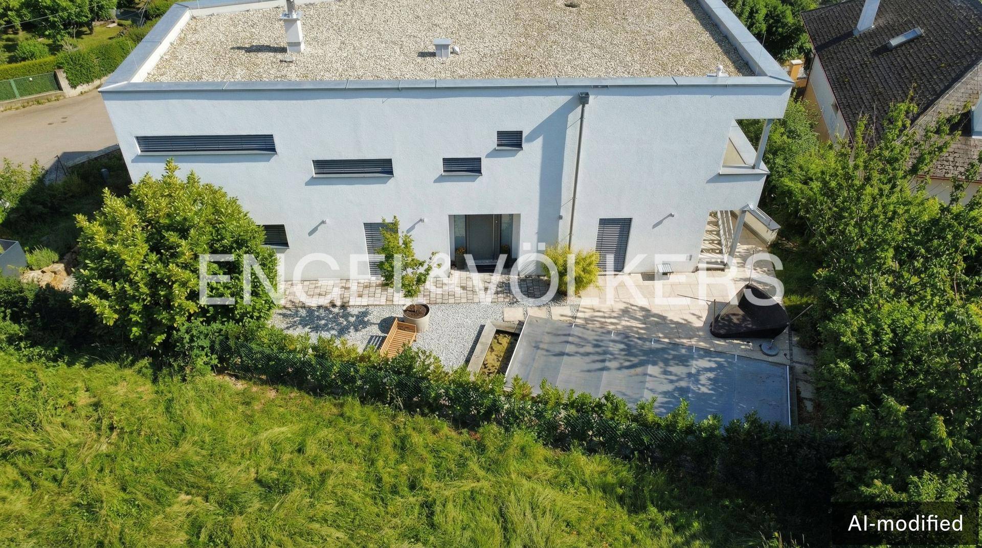 Rückansicht eines modernen Hauses mit Flachdach, gepflasterter Terrasse, Poolabdeckung und angrenzender Grünfläche.