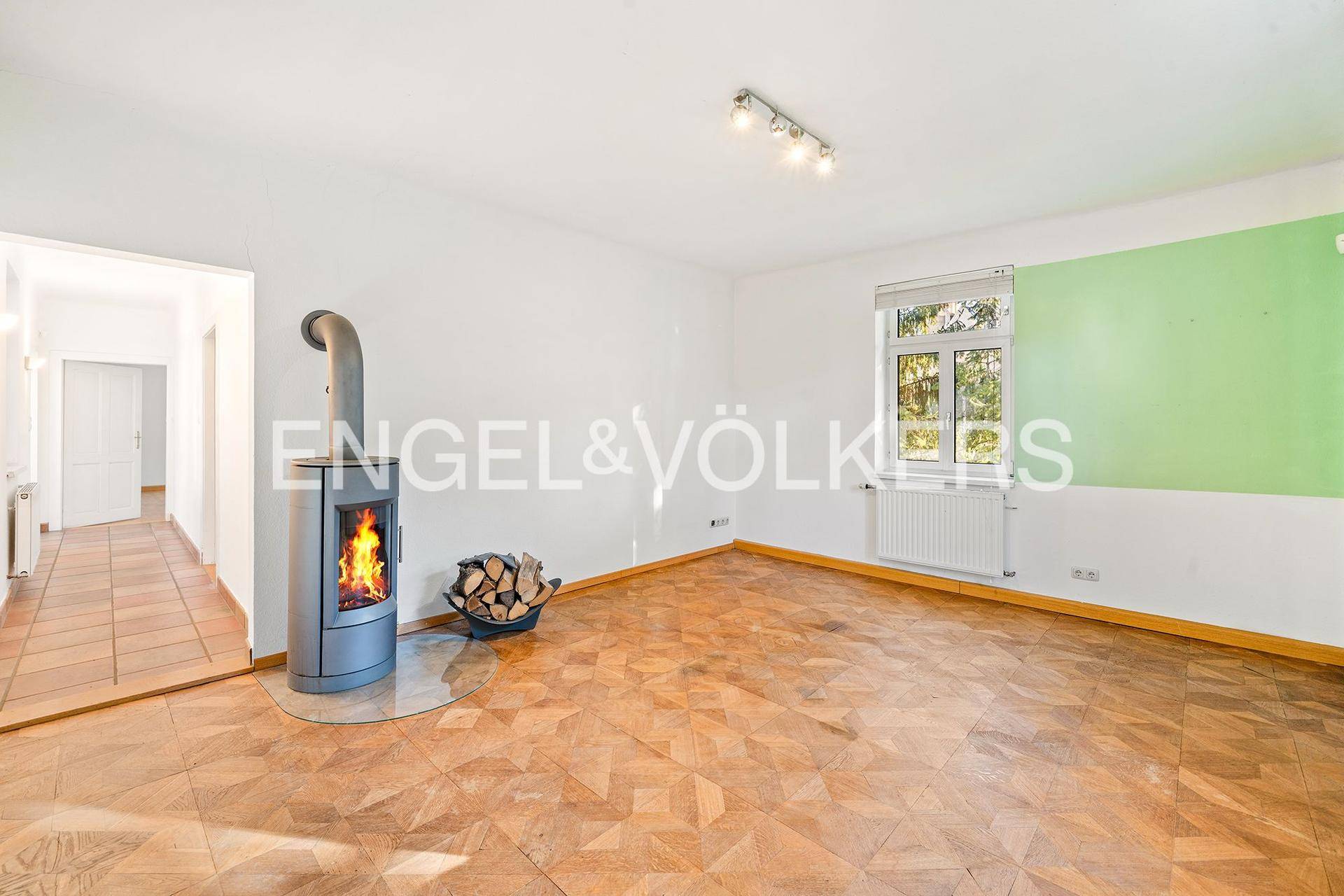 Helles Wohnzimmer mit Holzboden, modernem Holzofen und farbiger Akzentwand.