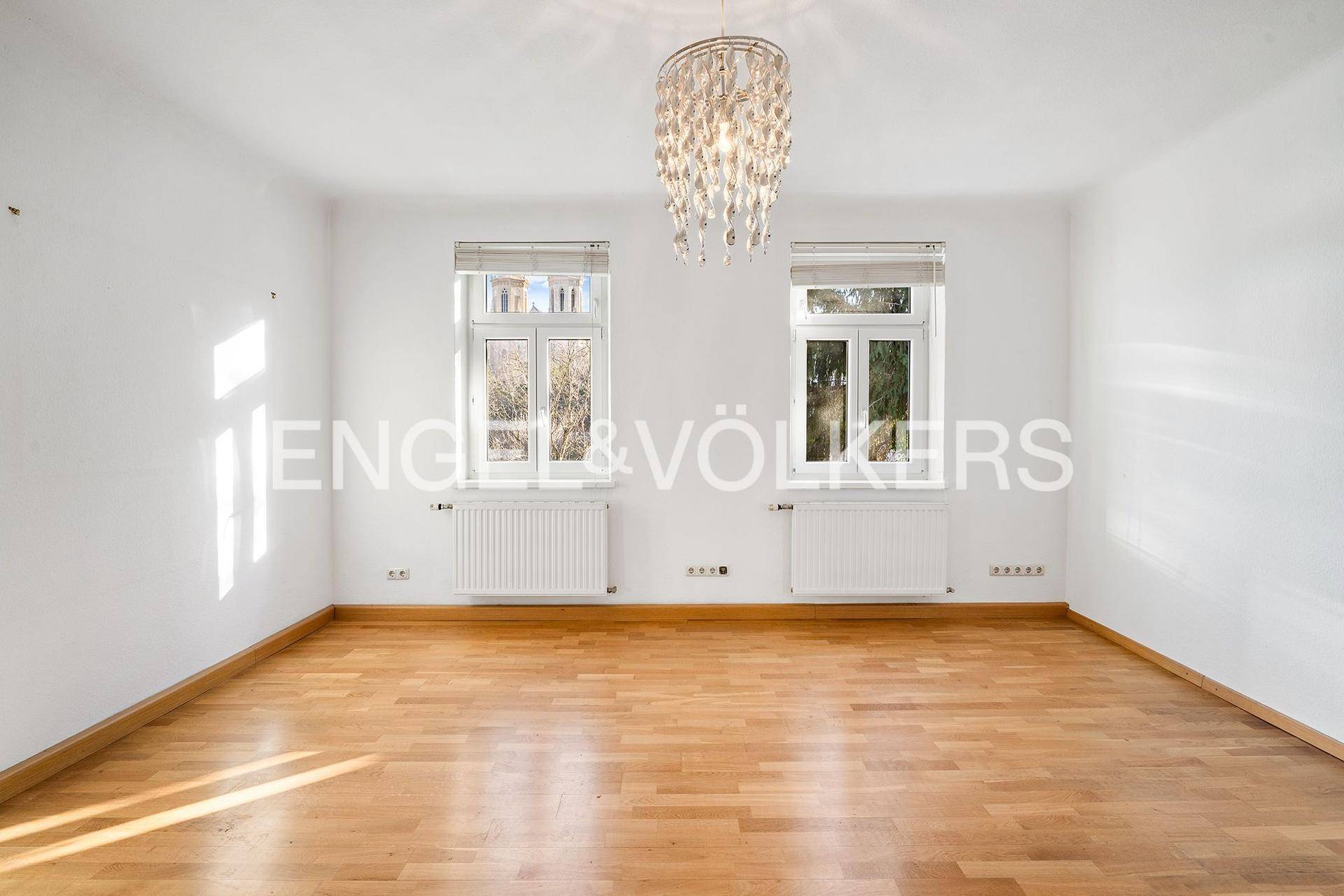 Helles, leeres Zimmer mit Holzboden und dekorativem Kronleuchter, ideal als Schlafzimmer.