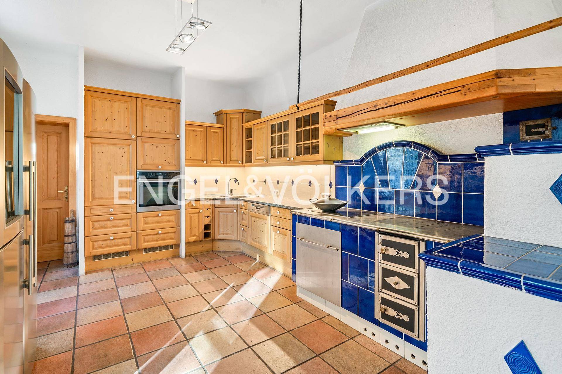 Rustikale Küche mit Holzschränken, blauen Fliesen und traditionellem Kachelofen.