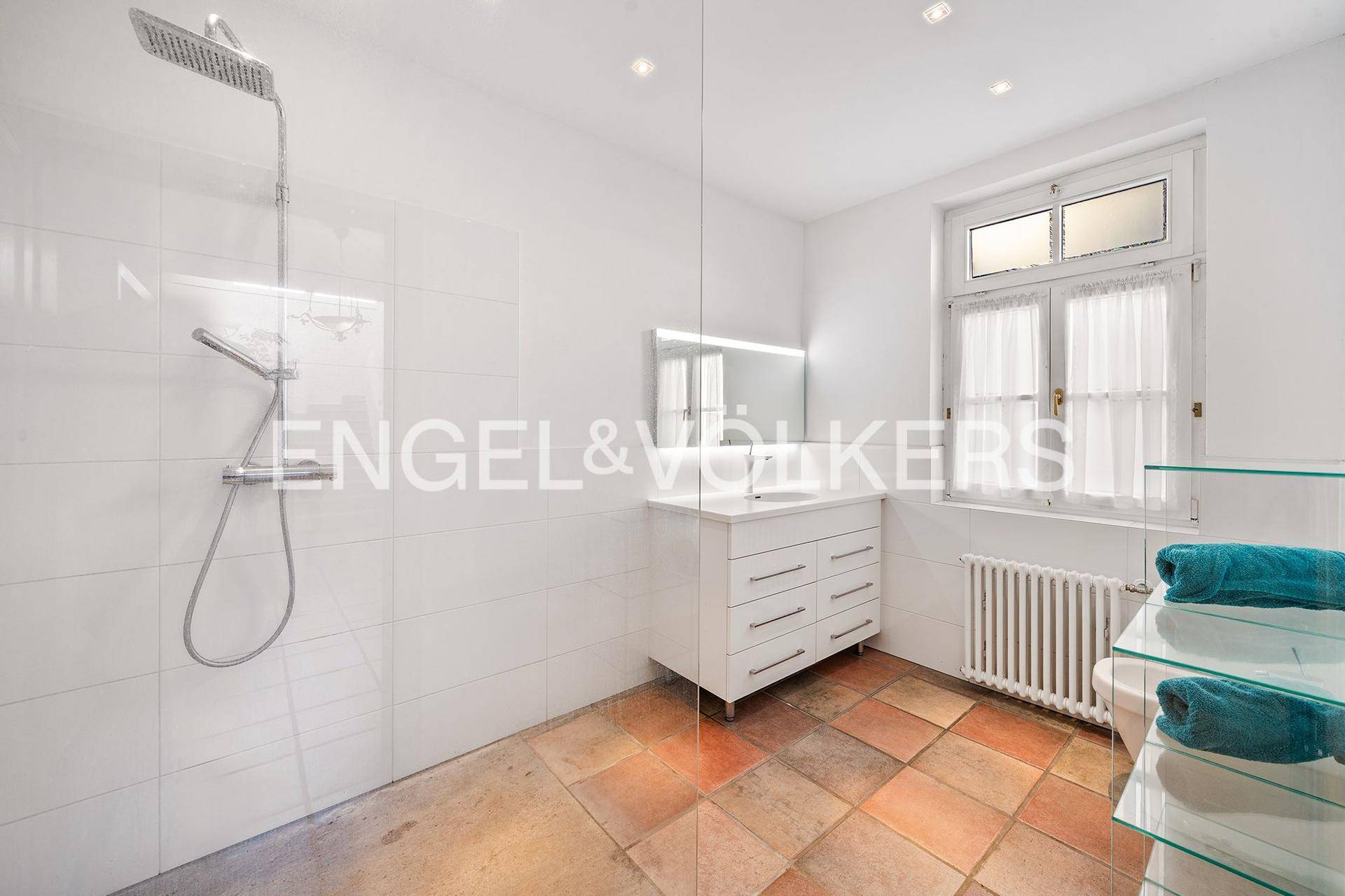 Modernes Badezimmer mit großer begehbarer Dusche, Waschtisch und Terrakotta-Fliesenboden.