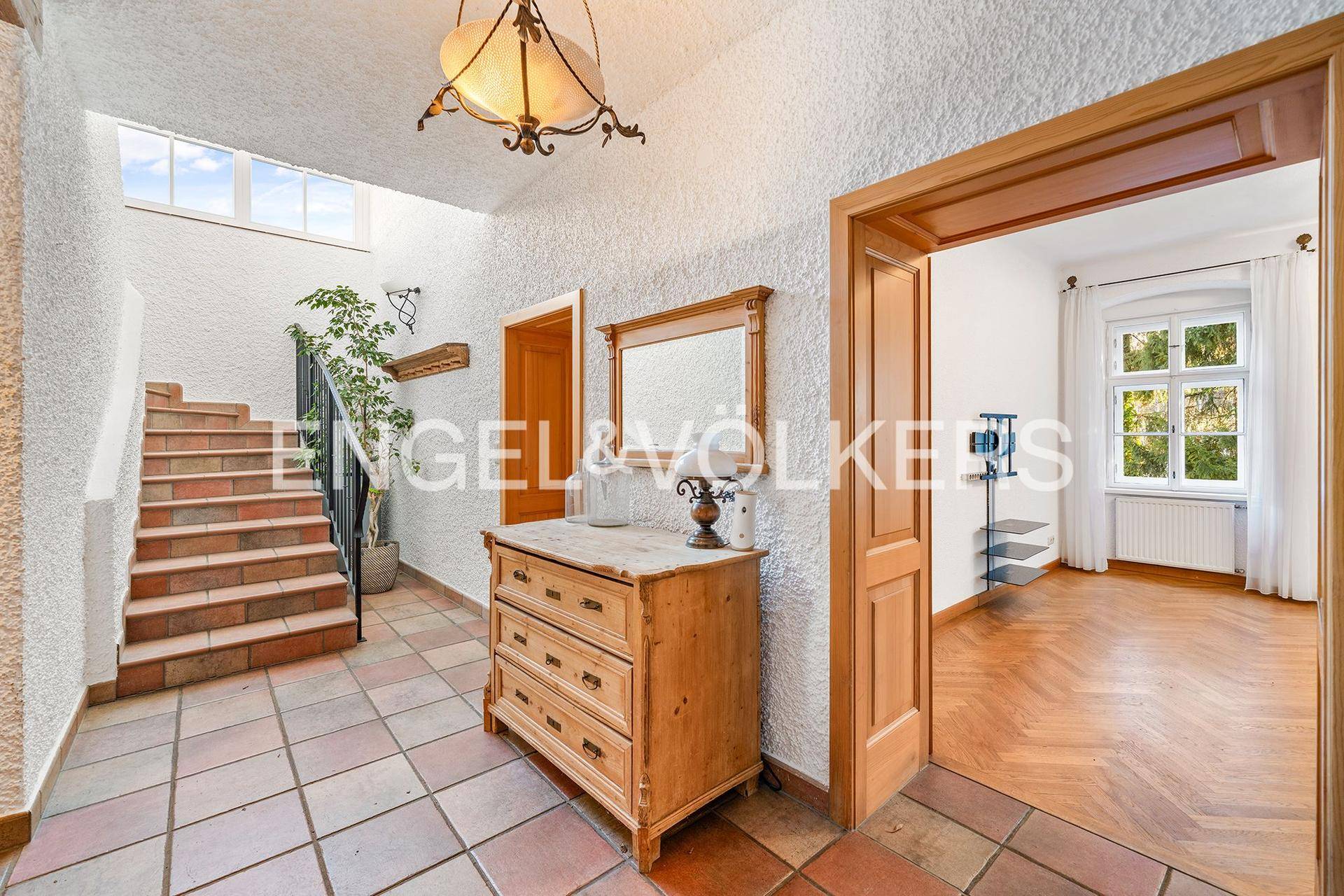 Geräumiger Eingangsbereich mit Terrakotta-Fliesenboden, Holzkommode und Treppe zum Obergeschoss.
