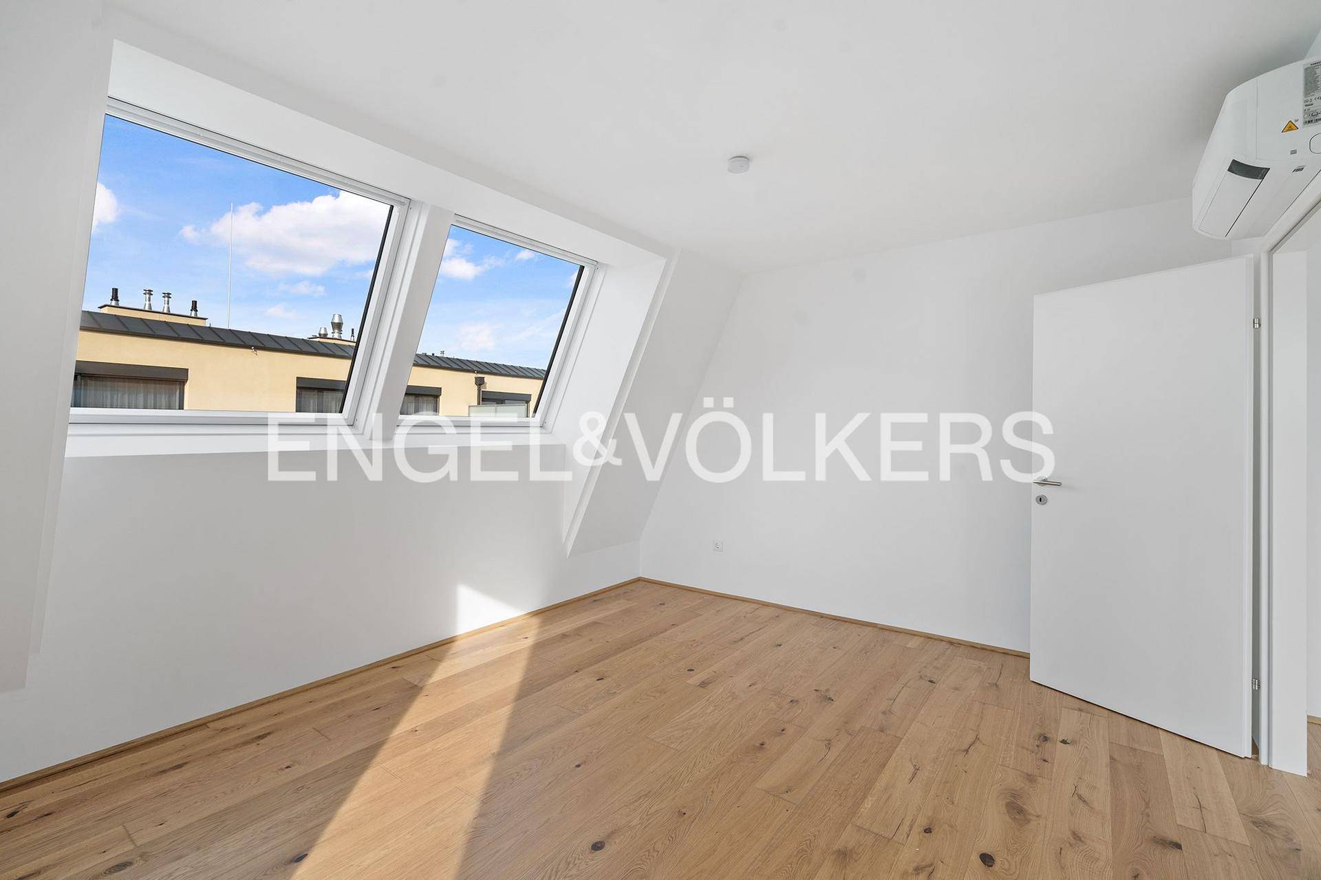 Leeres Schlafzimmer mit Holzboden, Dachfenstern und Klimaanlage.