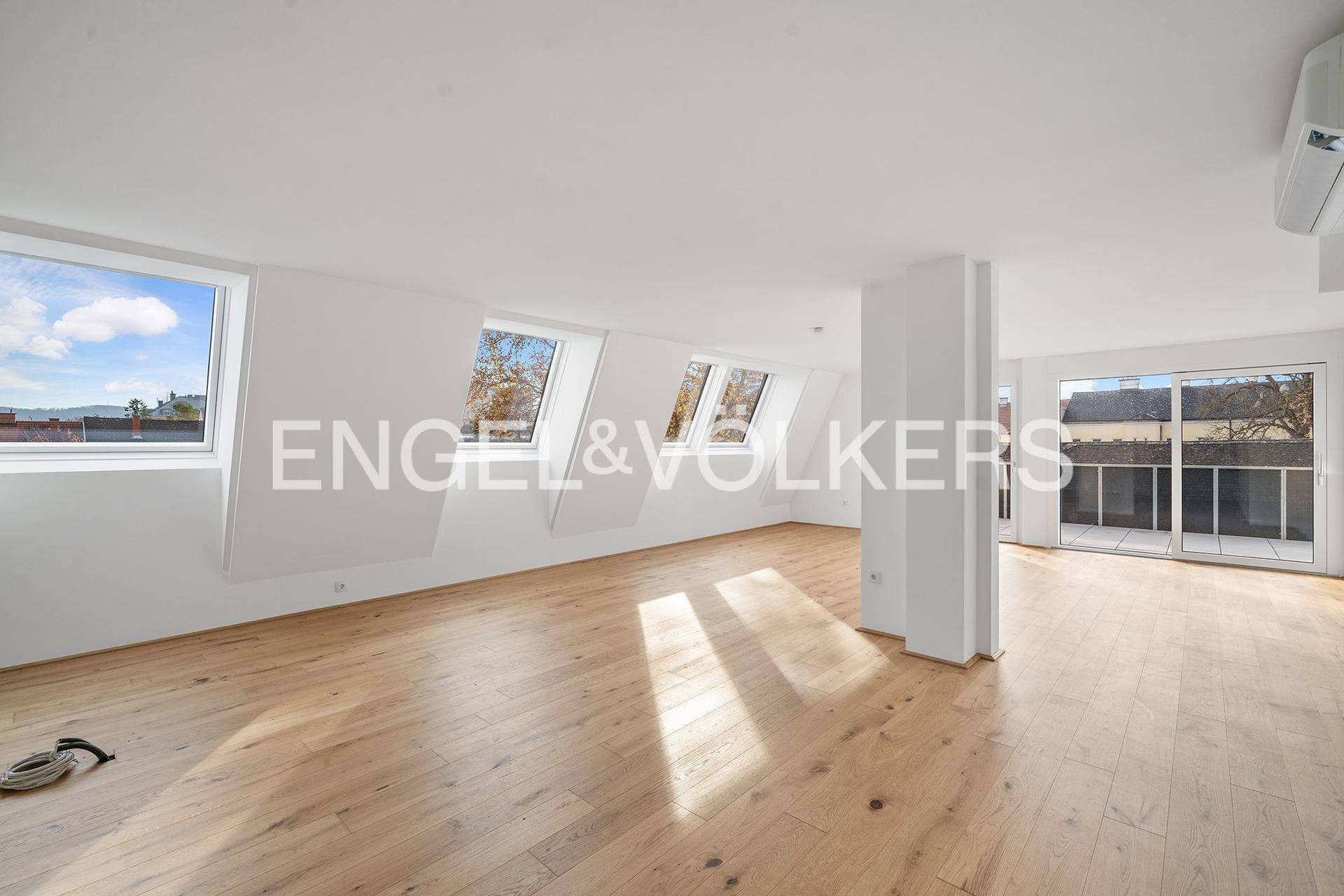 Großer, heller Wohnbereich mit Holzboden, Dachfenstern und Zugang zur Terrasse.