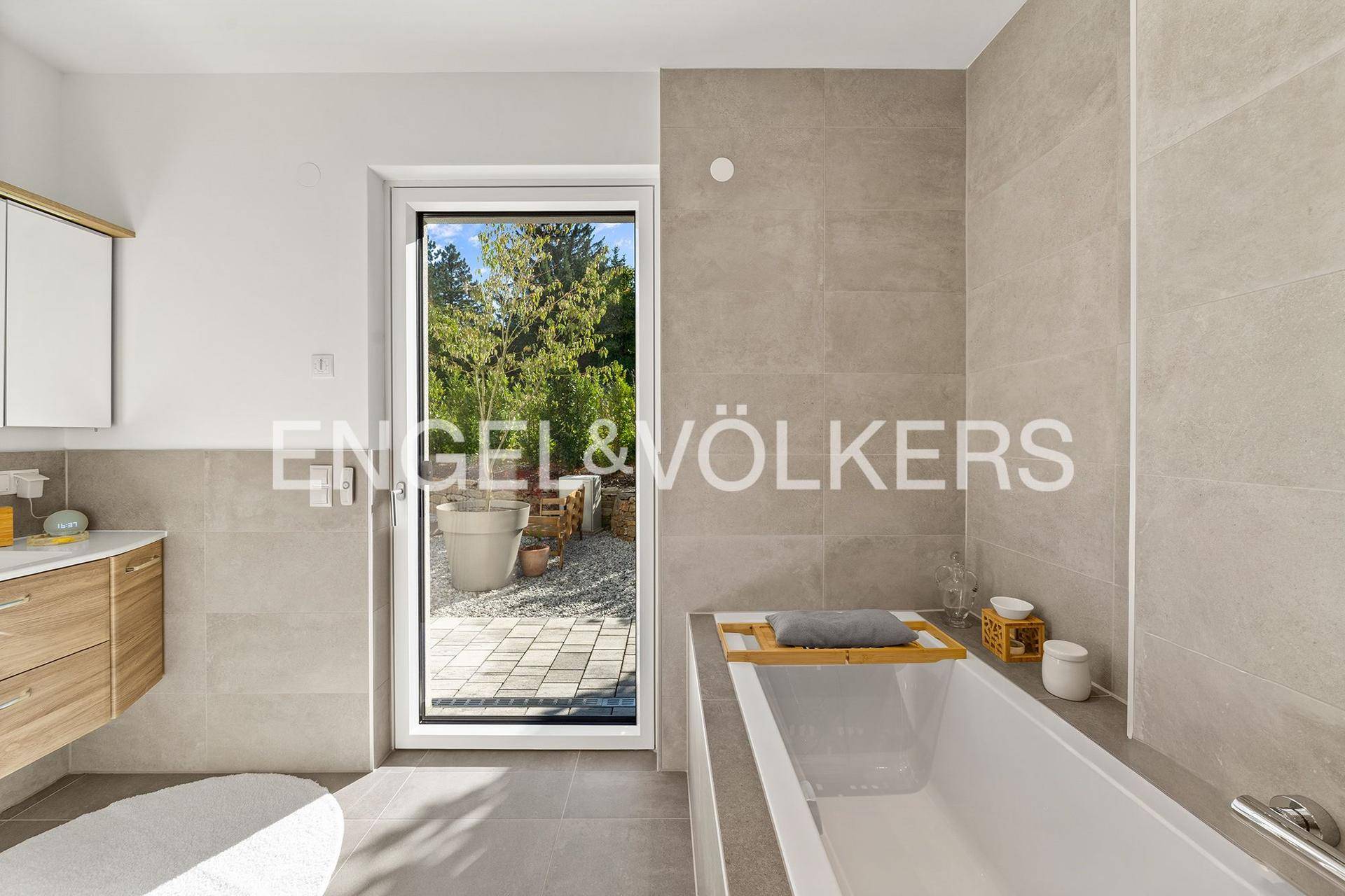 Modernes Badezimmer mit Badewanne, großformatigen Fliesen und Zugang zum Außenbereich.
