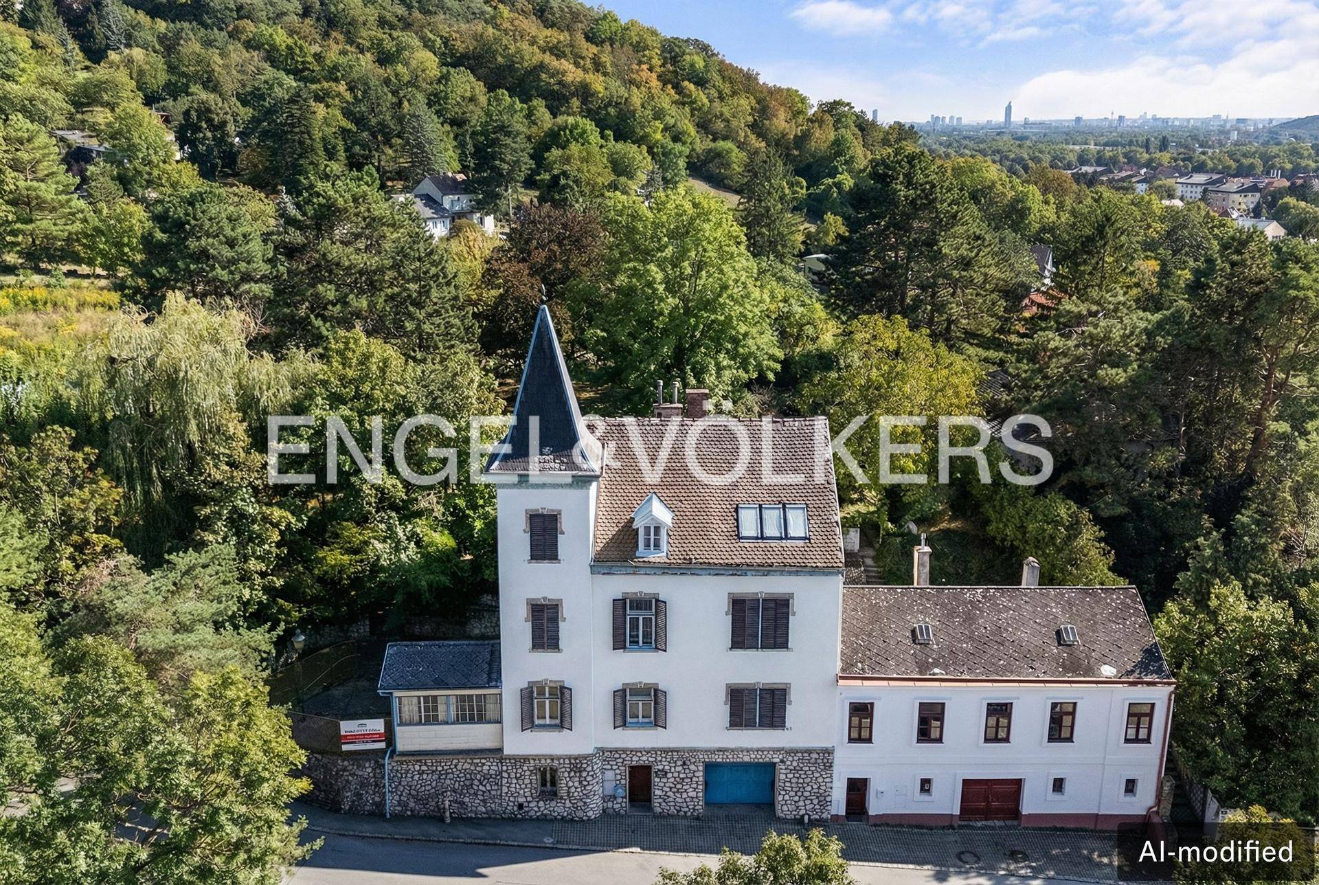 Luftaufnahme des historischen Gebäudes mit Turm, umgeben von viel Grün und Fernblick auf die Stadt.