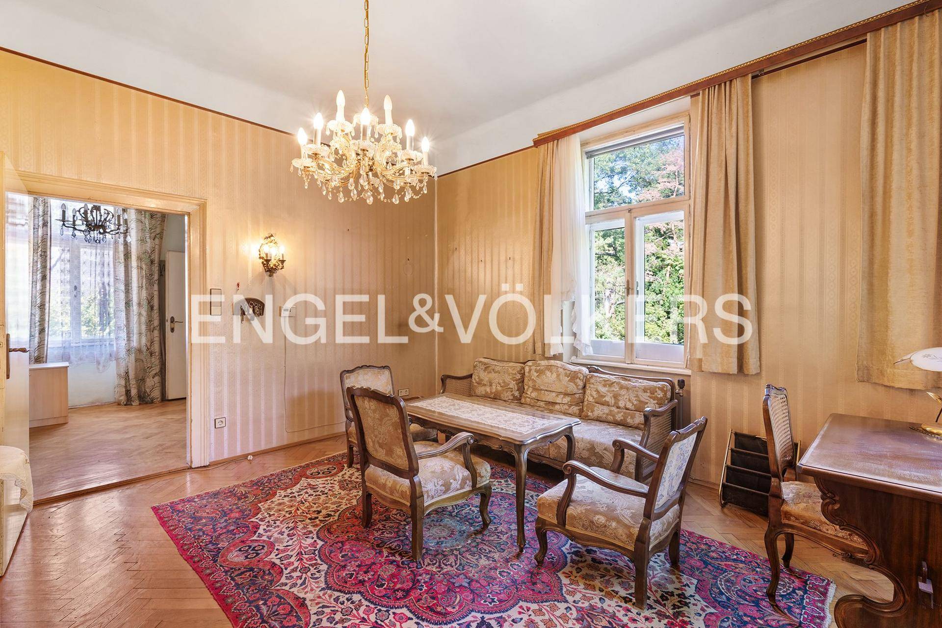 Klassisch eingerichtetes Wohnzimmer mit Kronleuchter, gemusterten Tapeten und Holzboden.