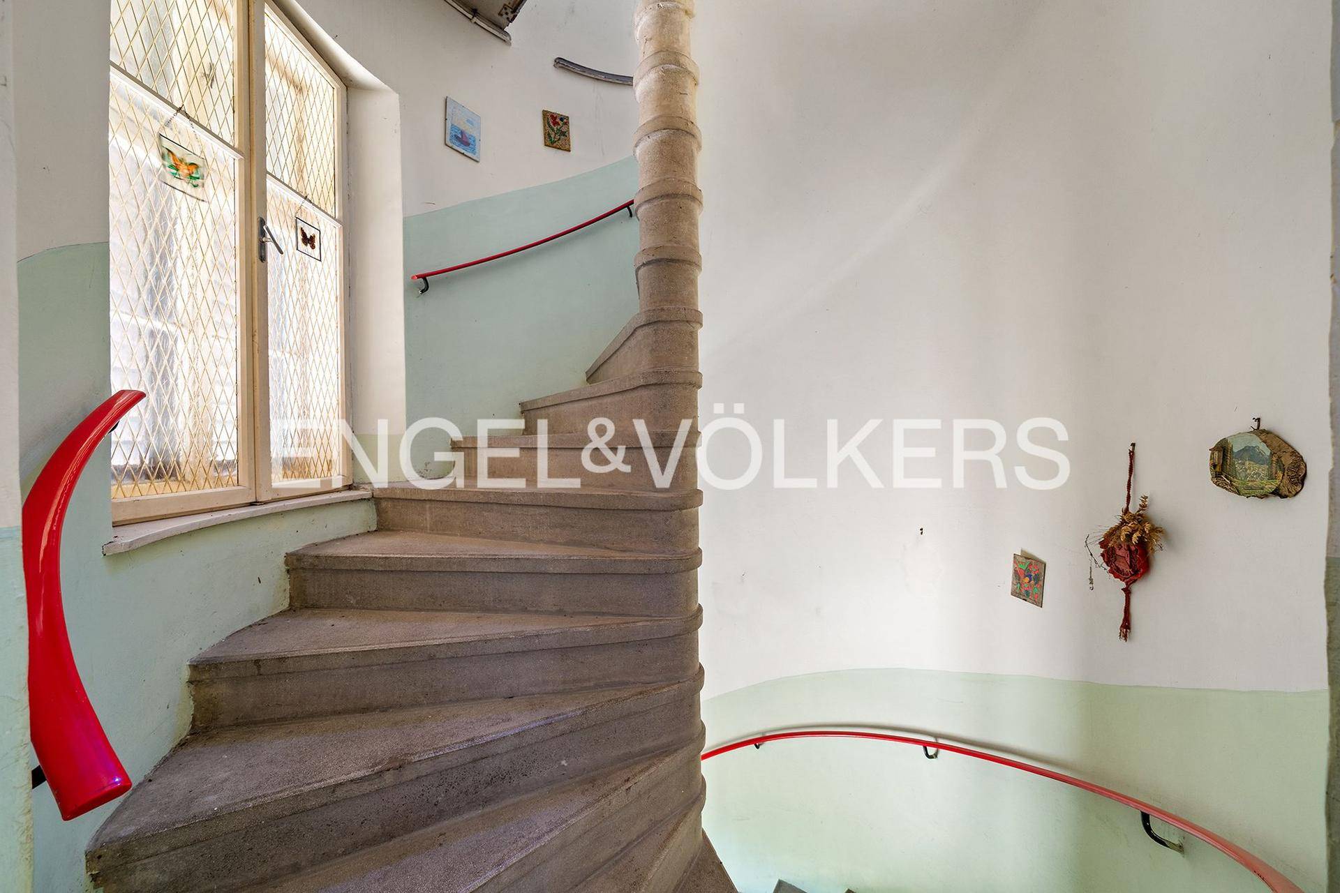 Historische Wendeltreppe mit Bleiglasfenster und zweifarbigen Wänden in einem Altbau.