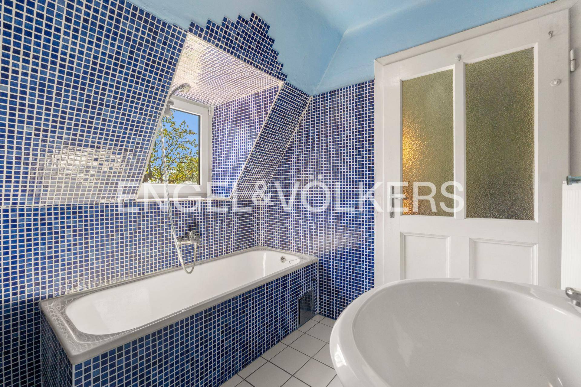 Badezimmer mit blauen Mosaikfliesen, Badewanne, Waschbecken und einem Fenster.