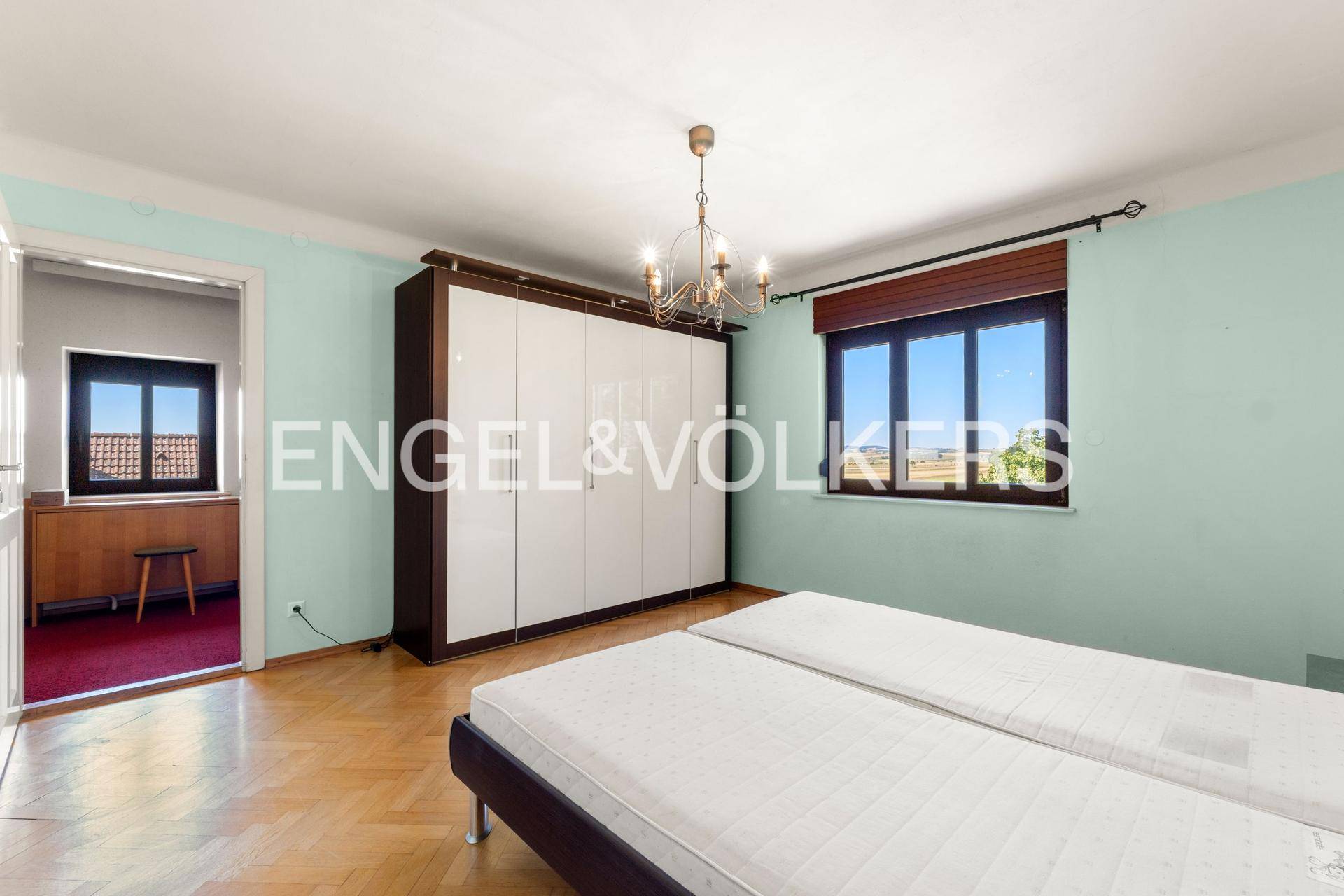 Schlafzimmer mit hellblauen Wänden, Parkettboden, großem Kleiderschrank und Fenster.
