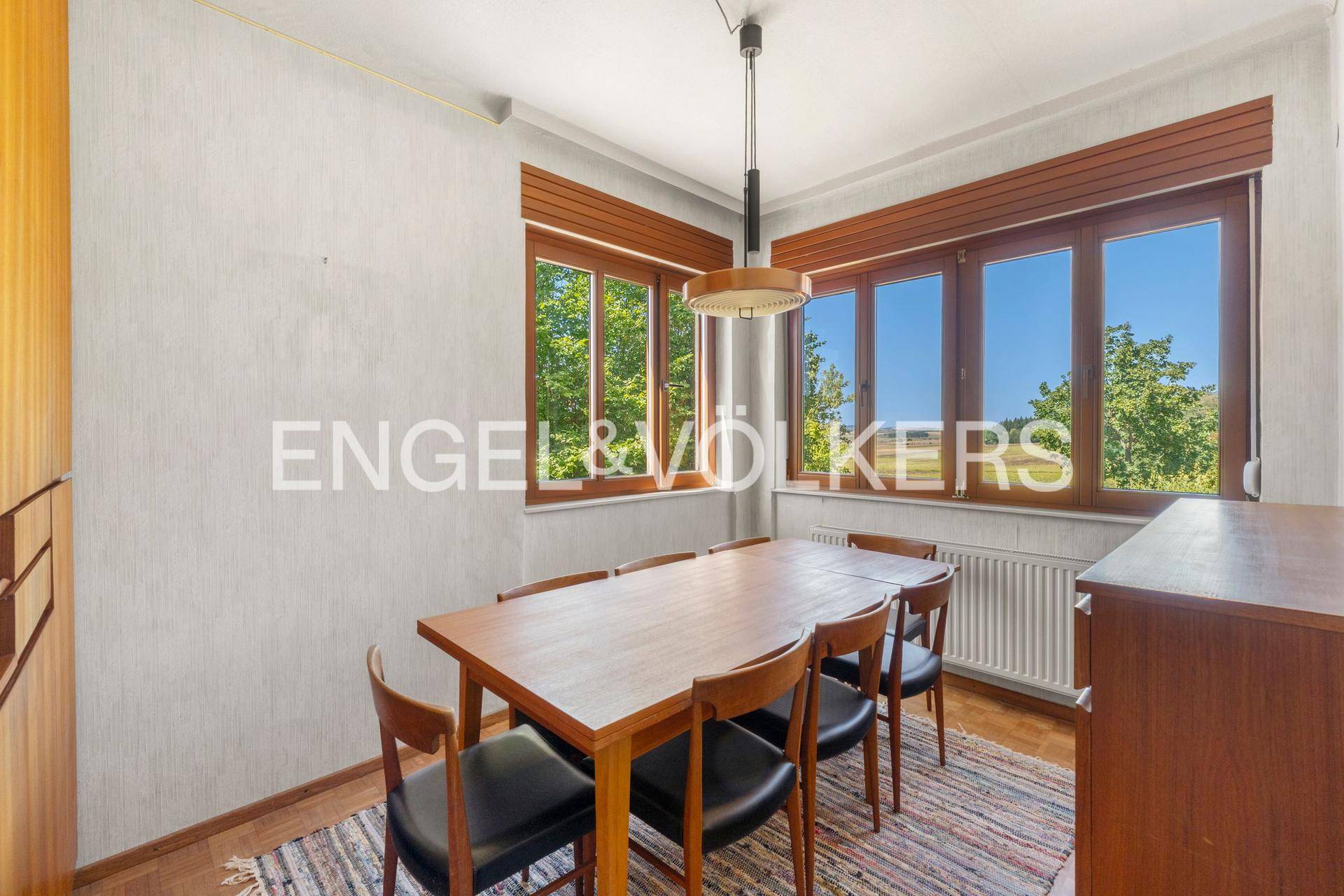 Esszimmer mit Holztisch und Stühlen, Parkettboden und viel Tageslicht durch große Fenster.