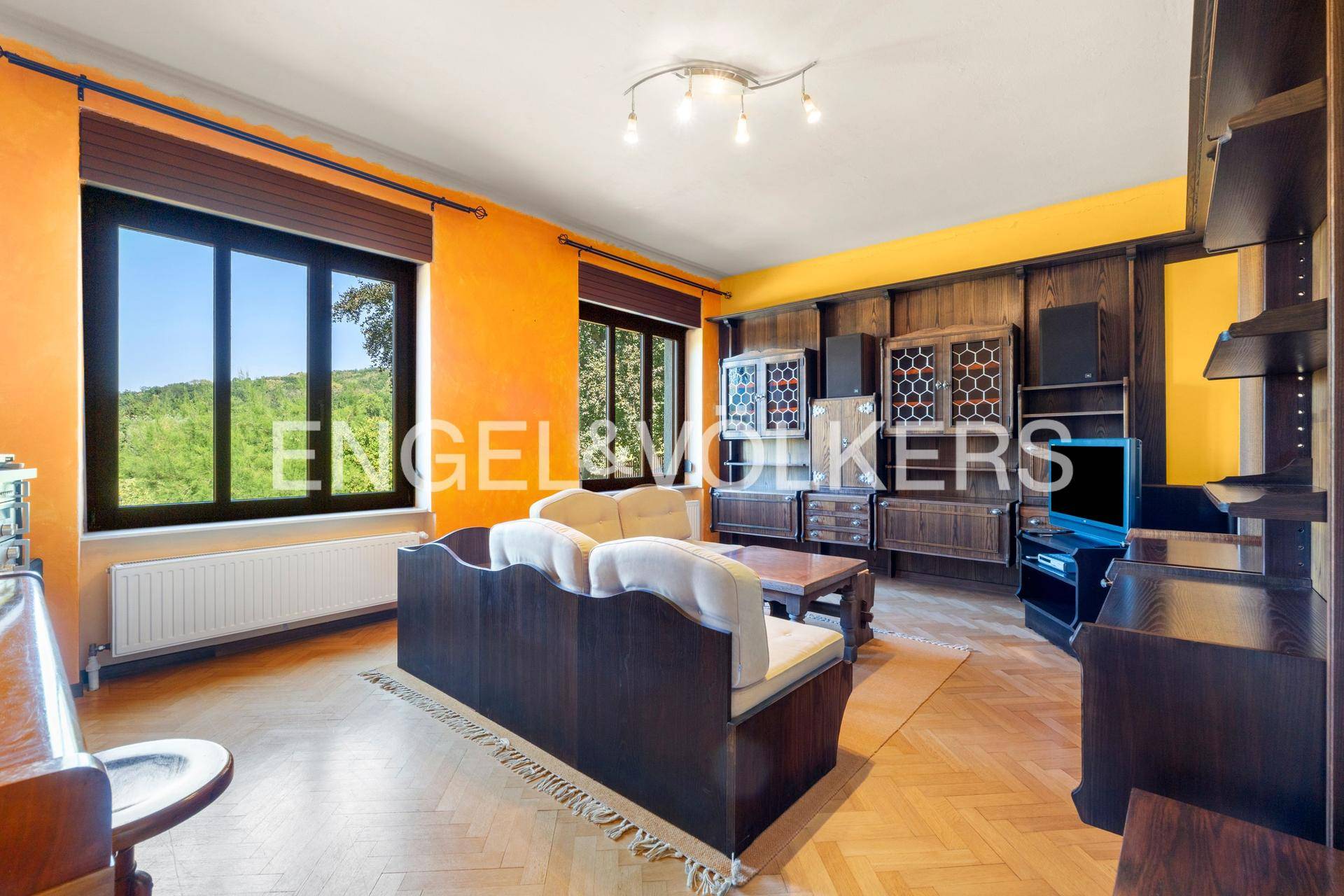 Gemütliches Wohnzimmer mit orangefarbenen Wänden, Holzmöbeln und Blick ins Grüne.