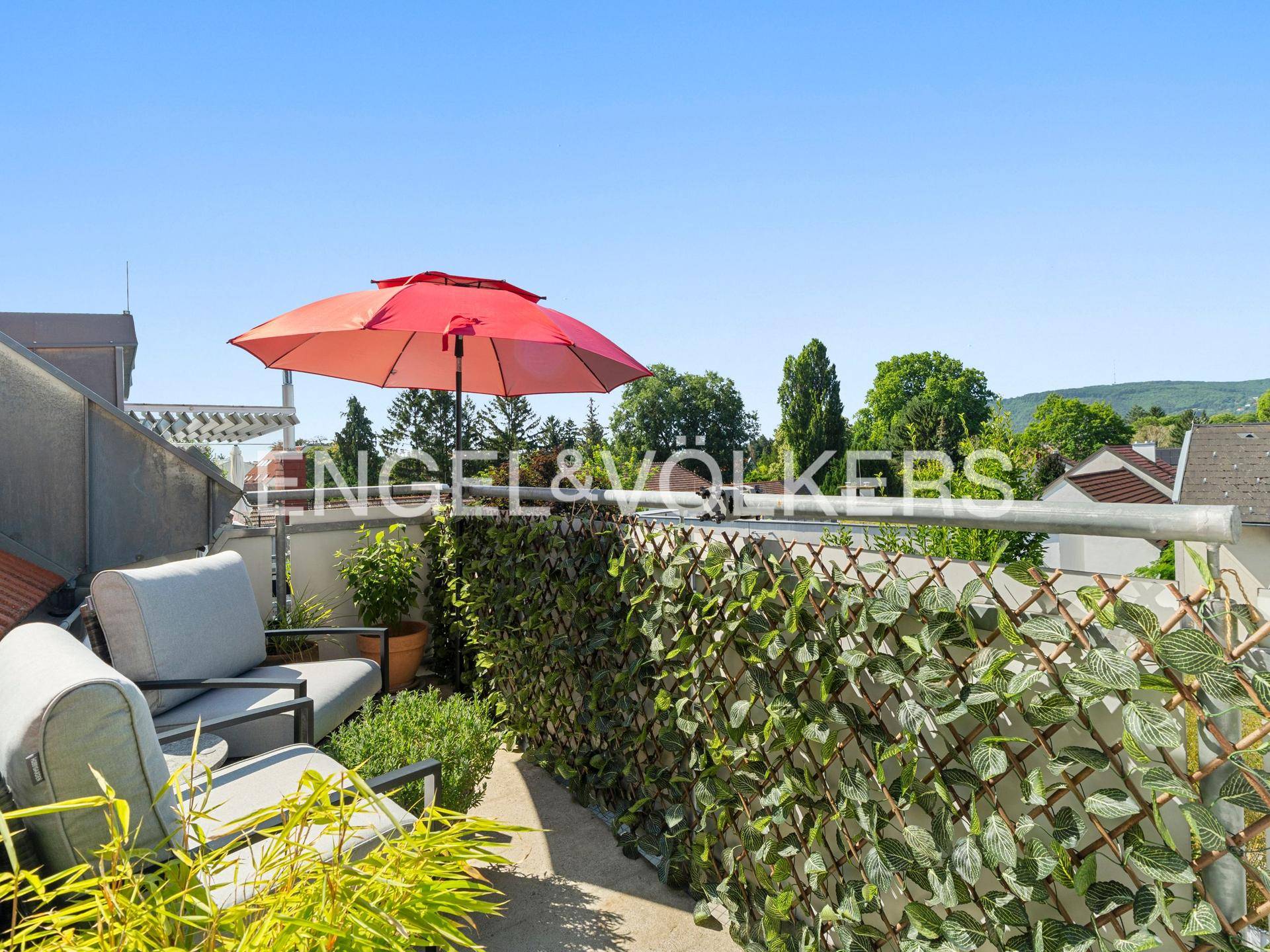 Gemütlicher Balkon mit Sitzgelegenheiten, Sonnenschirm und grüner Bepflanzung.