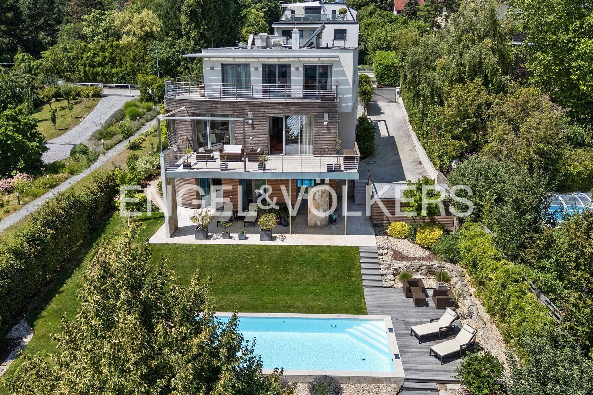 Luftaufnahme einer modernen Villa mit großem Poolbereich und weitläufigem Garten in grüner Umgebung.