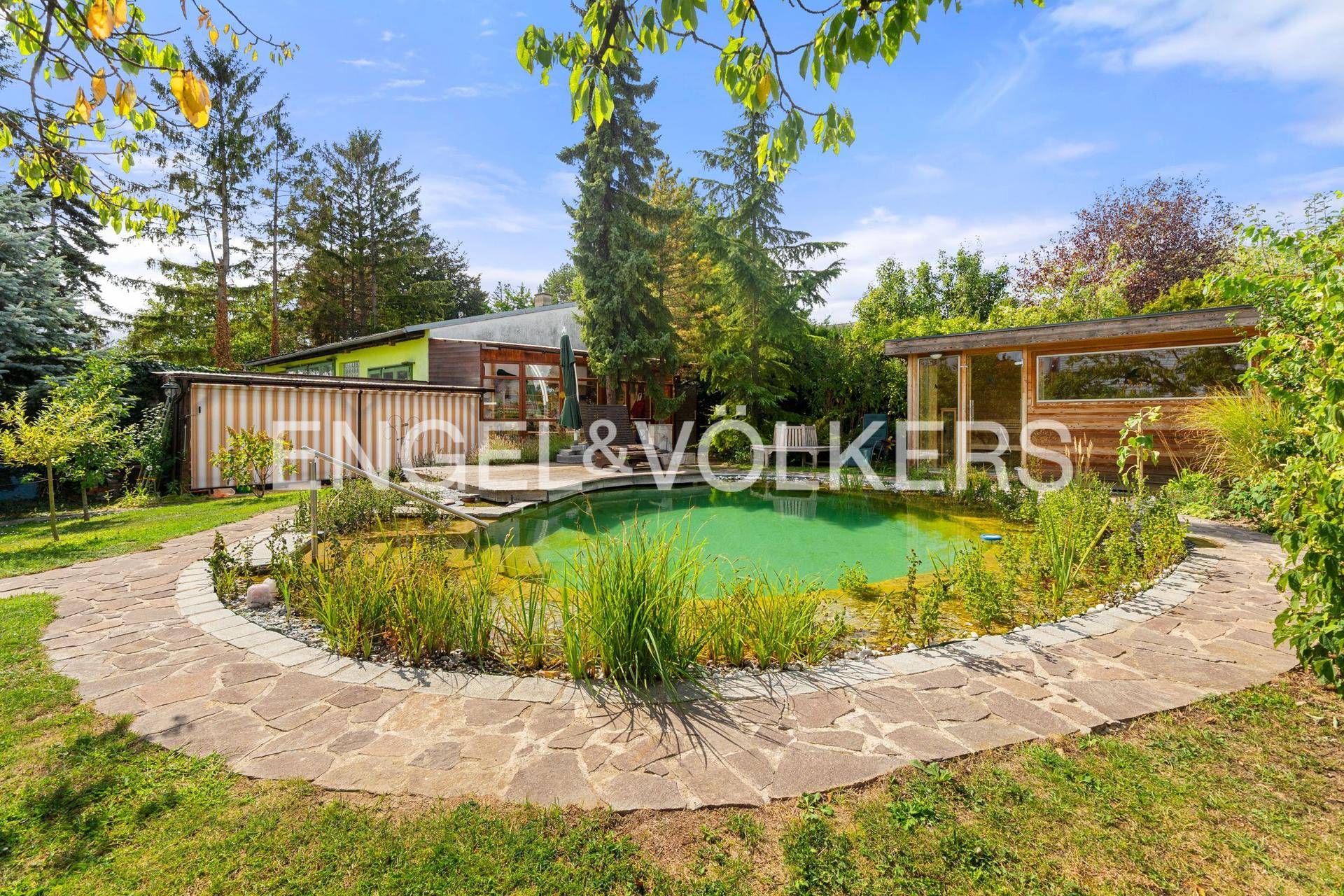 Weitläufiger Garten mit Naturteich, Steinpfad und dem Wohnhaus im Hintergrund.