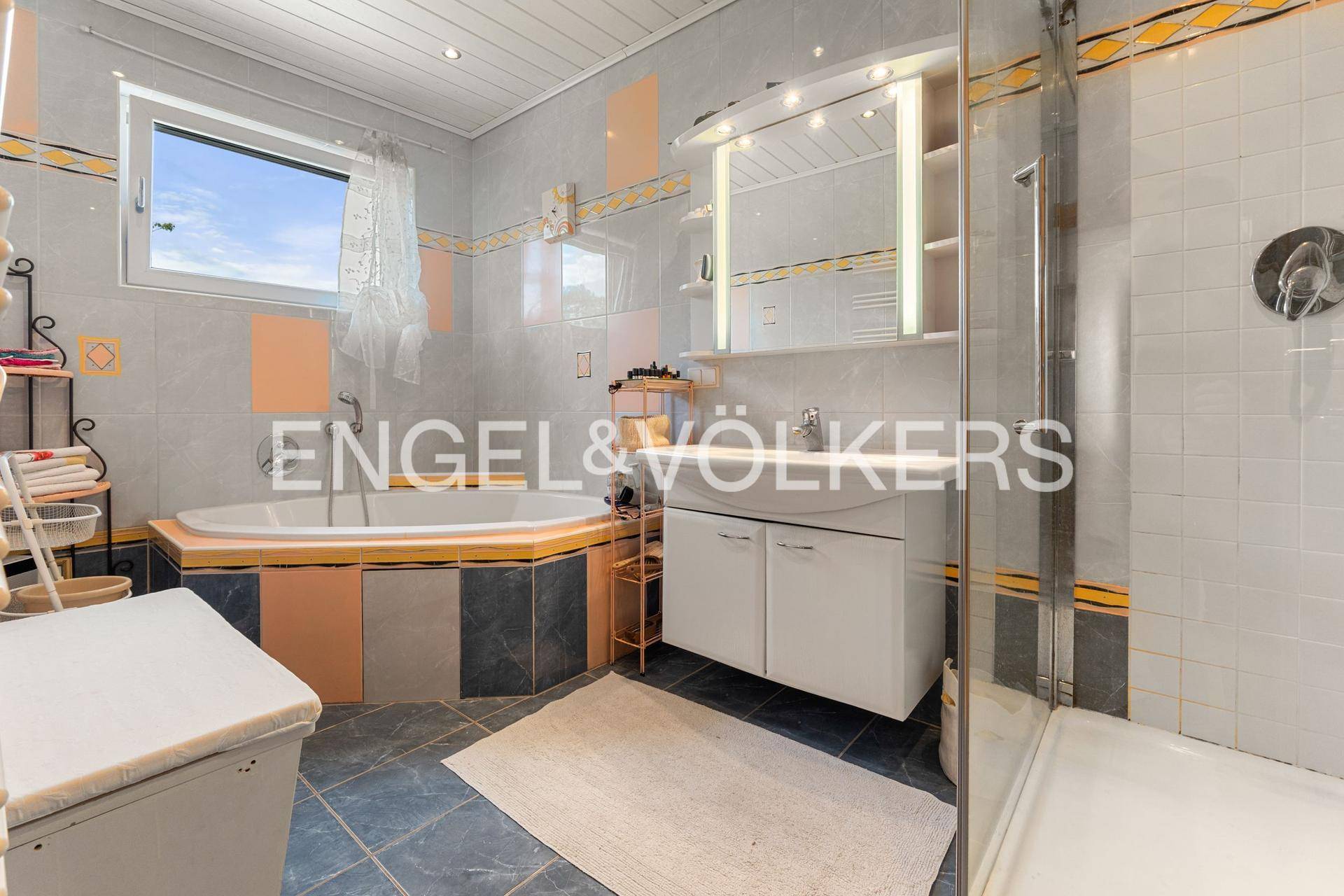 Badezimmer mit grauen und orangefarbenen Fliesen, Eckbadewanne und separater Duschkabine.