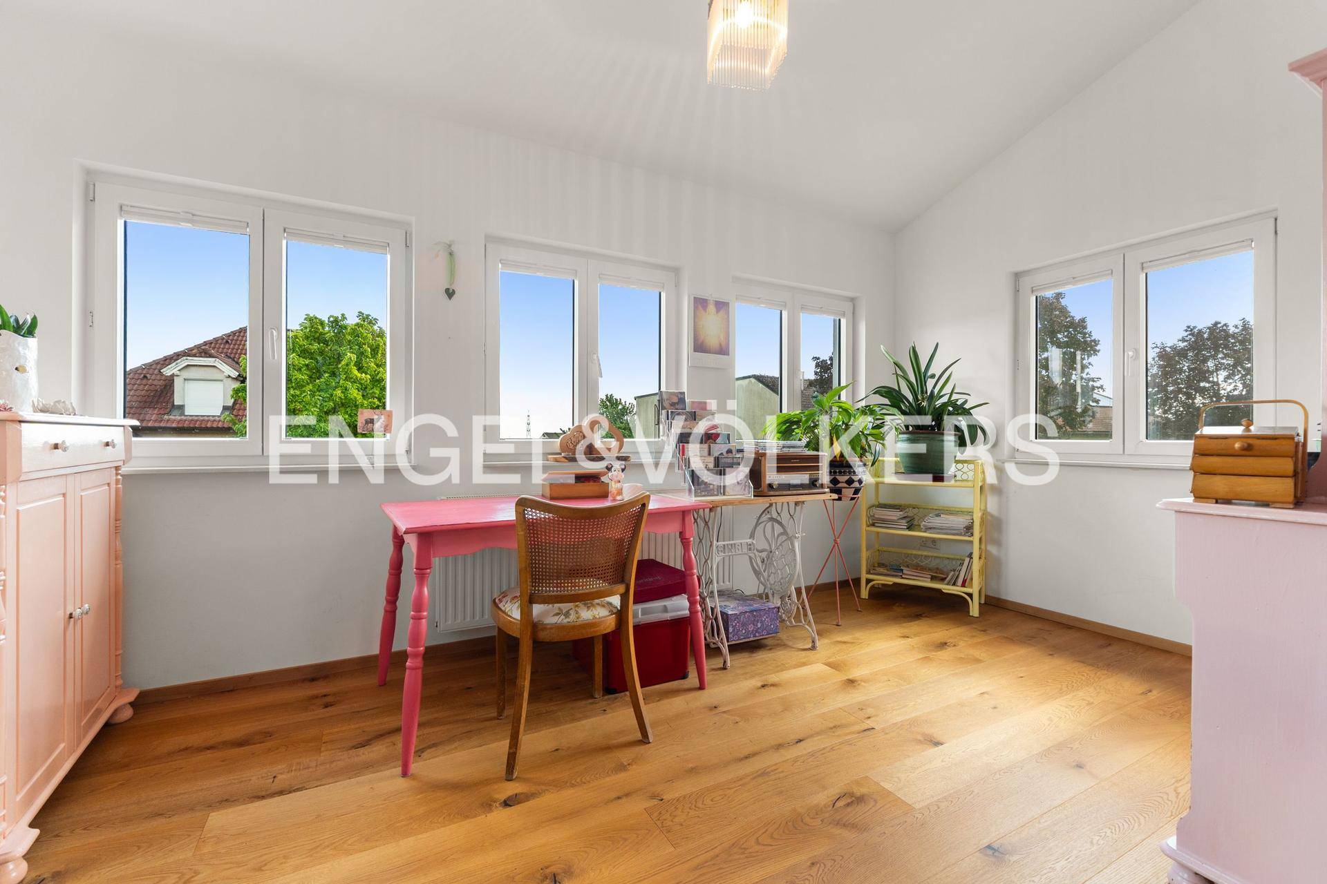 Helles Arbeitszimmer mit vielen Fenstern, Holzboden und einem farbenfrohen Schreibtisch.