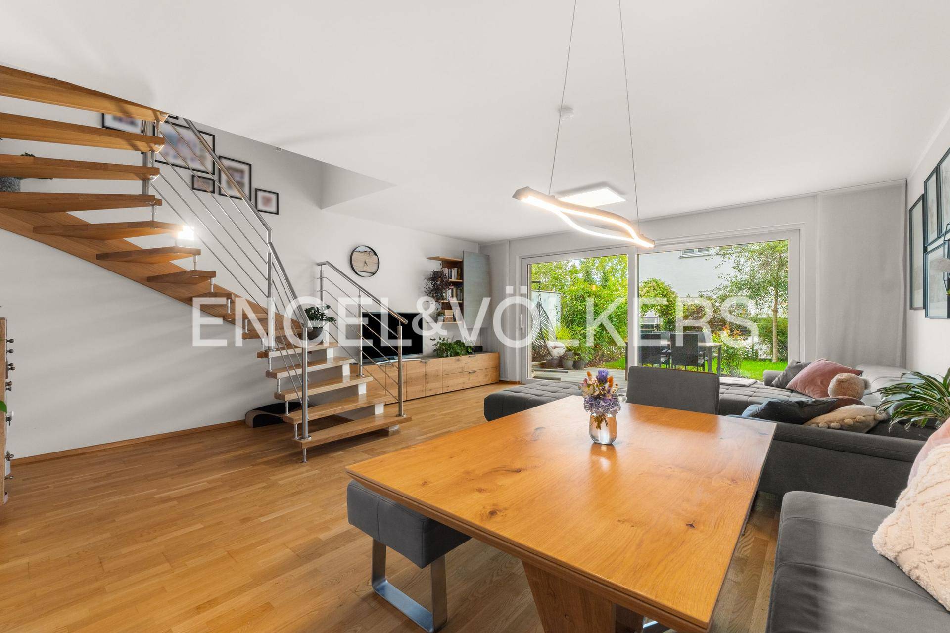 Geräumiger Wohn- und Essbereich mit offener Holztreppe und Blick in den Garten.