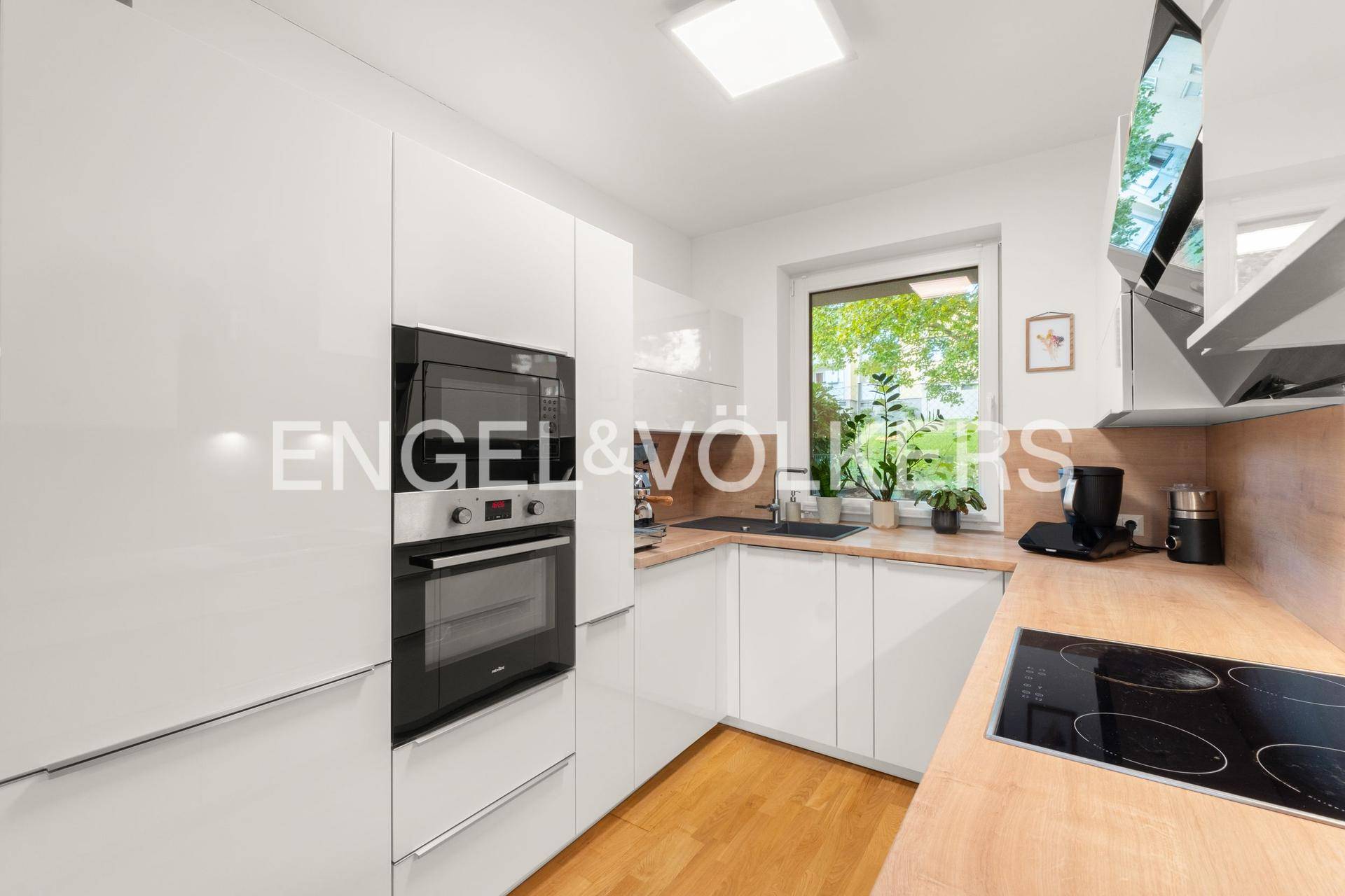 Moderne Küche mit weißen Hochglanzfronten, Holzarbeitsplatten und Einbaugeräten.