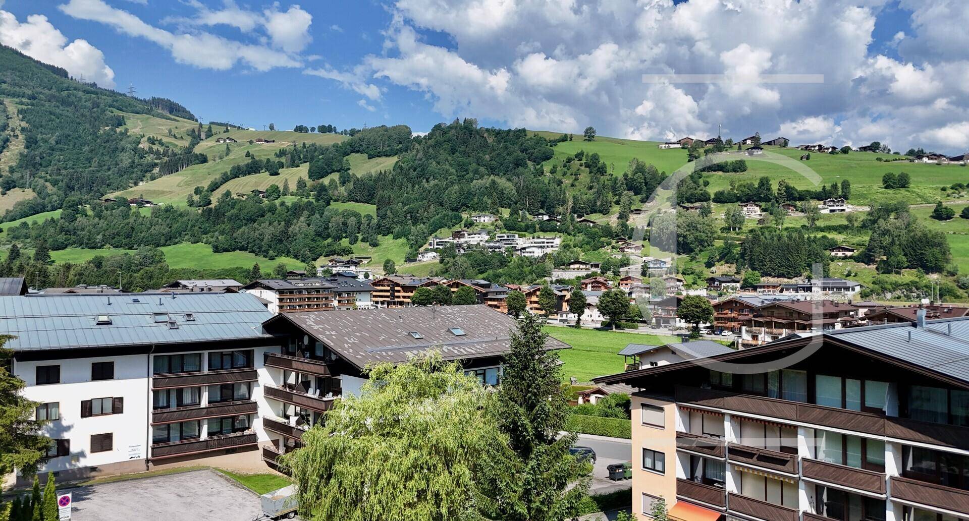 Panoramablick über ein alpines Dorf mit traditionellen Häusern, eingebettet in grüne Hügel und Berge.