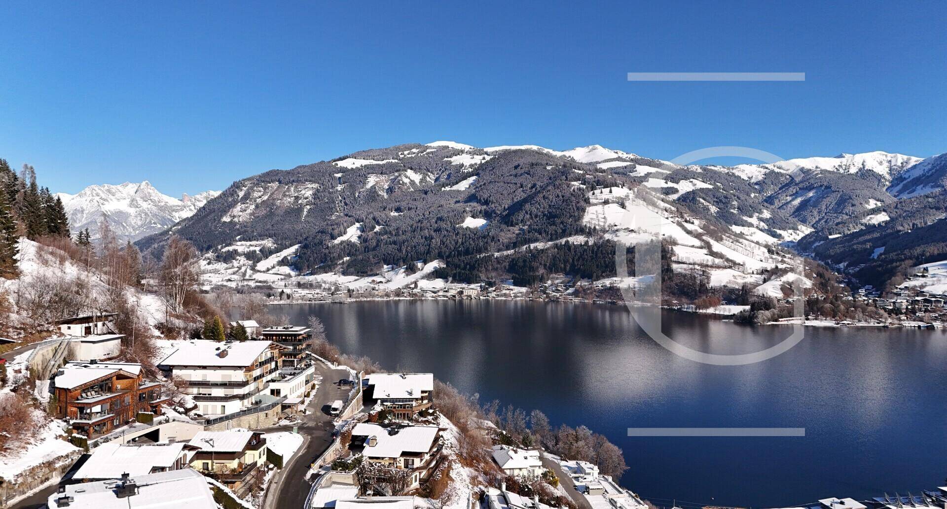 Panoramablick auf einen See umgeben von schneebedeckten Bergen und einer kleinen Ortschaft am Ufer.