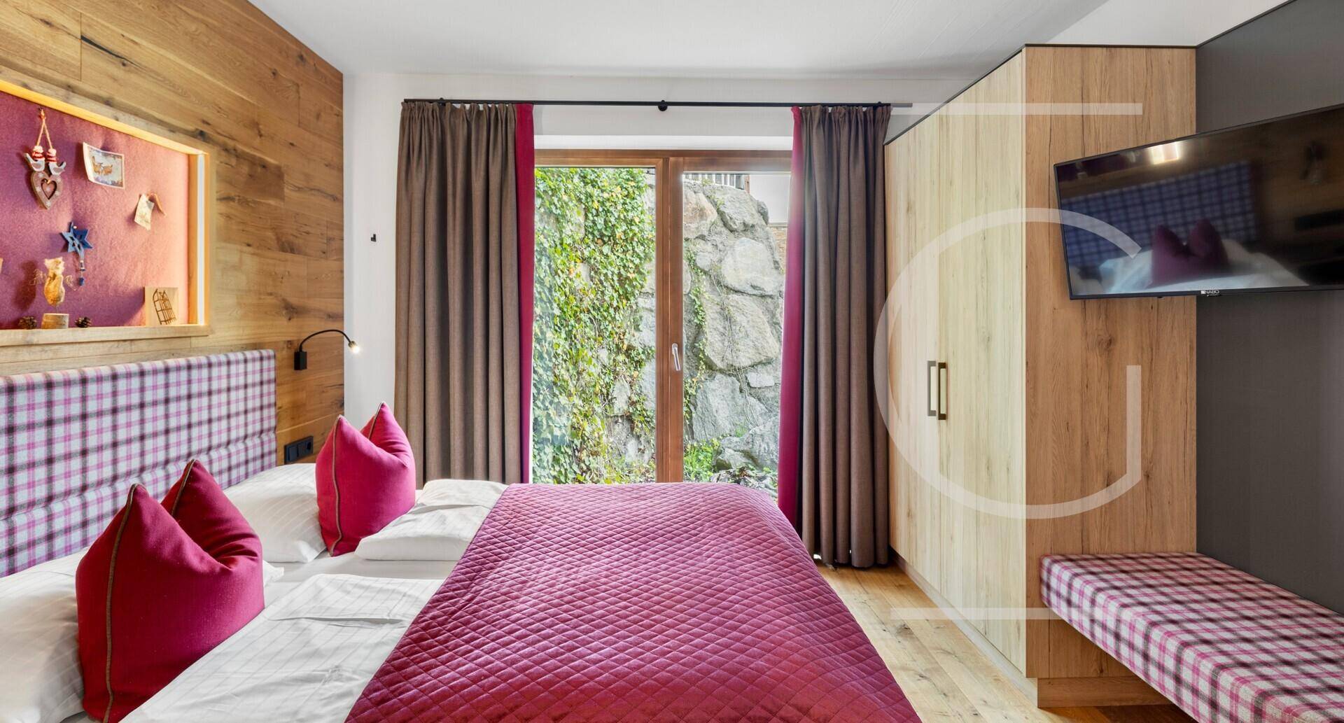 Gemütliches Schlafzimmer mit Doppelbett, Holzwand und Blick auf die Felsen und Bäume.